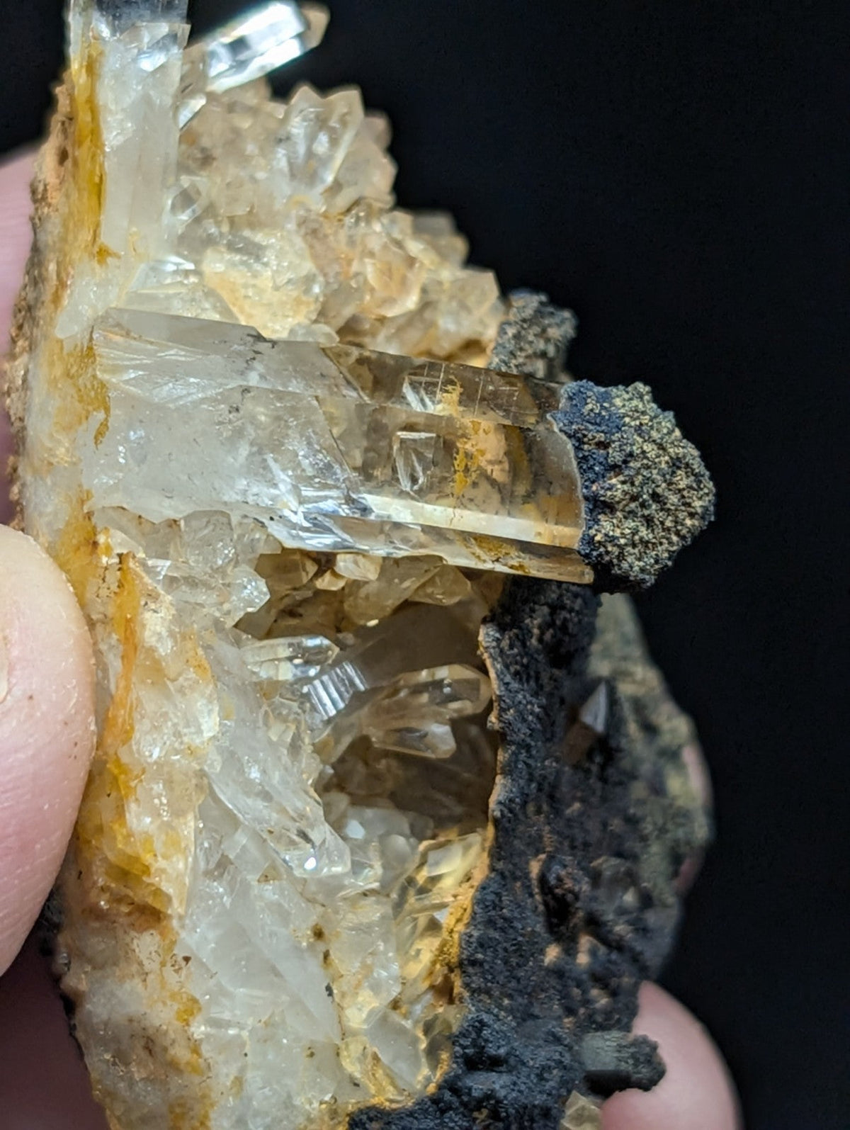 A translucent, amber-hued quartz crystal cluster with sharp facets and a rough, dark matrix base.