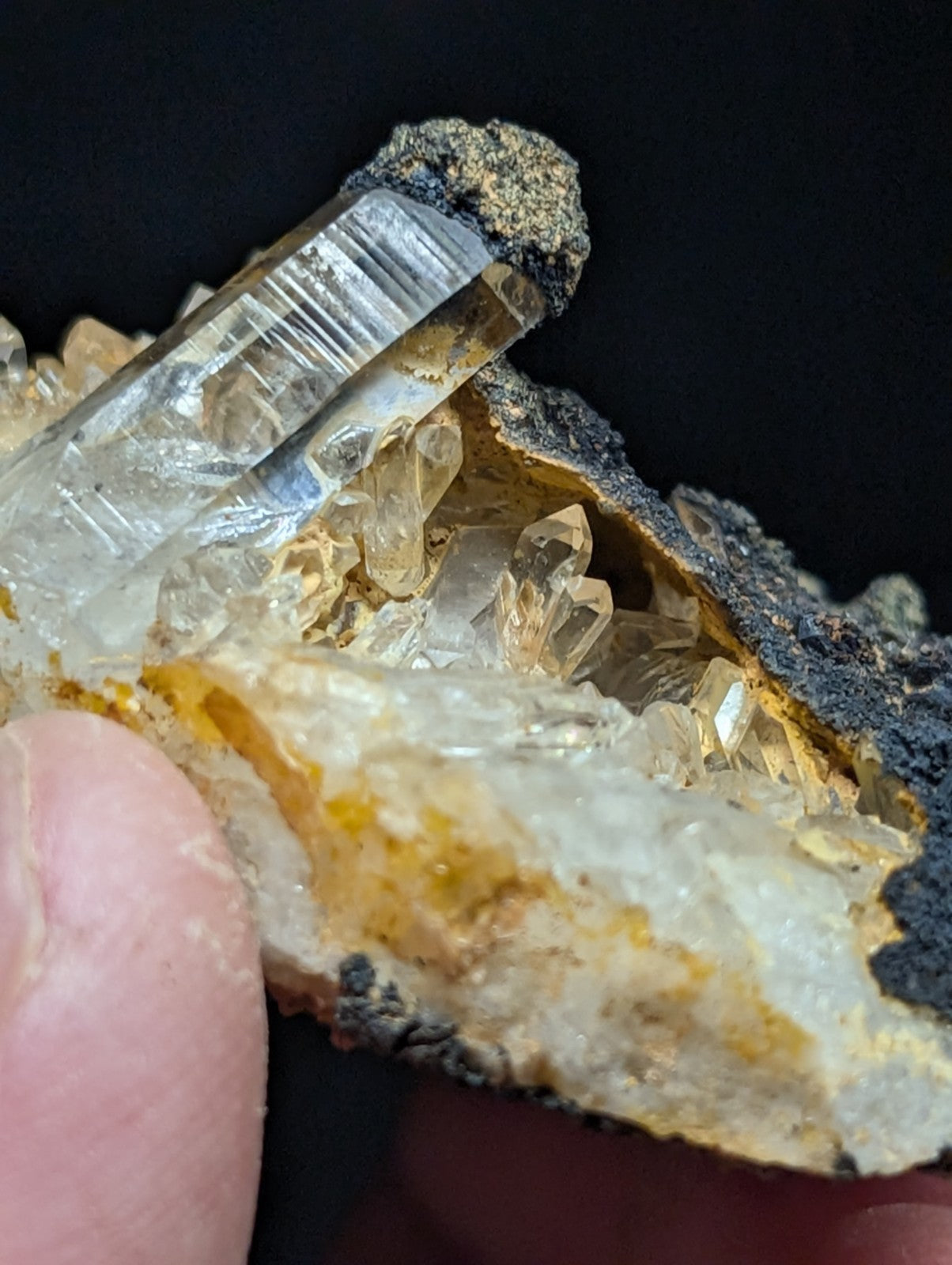 A translucent, clear quartz crystal cluster with golden-yellow inclusions and a rough, dark matrix base.