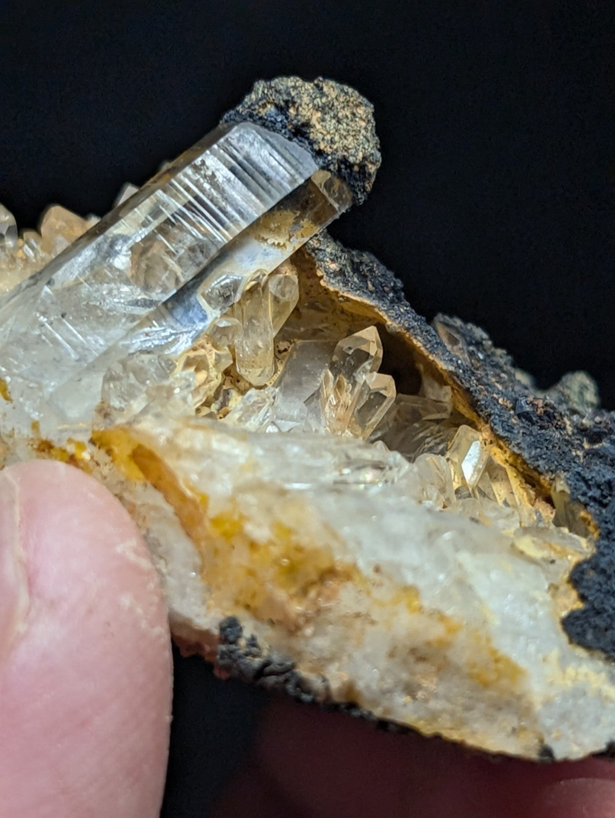 A translucent, clear quartz crystal cluster with golden-yellow inclusions and a rough, dark matrix base.