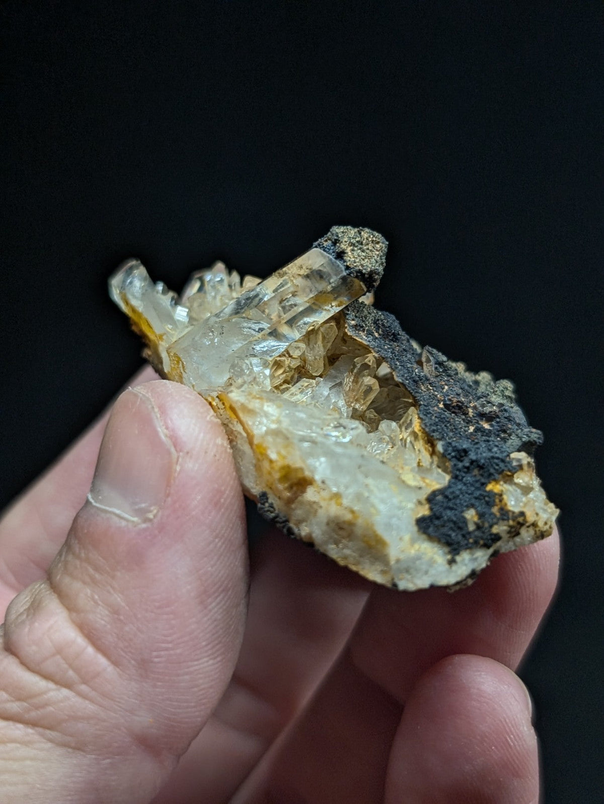 A translucent, crystalline mineral specimen with clear and yellowish quartz crystals growing from a dark, earthy matrix.