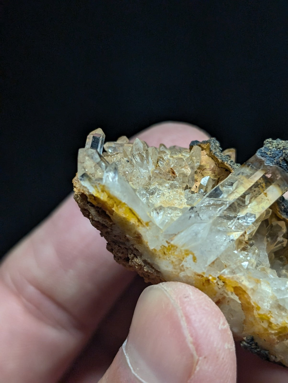 A translucent quartz crystal cluster with sharp, clear points emerging from a rugged, earthy matrix of yellow and brown mineral.