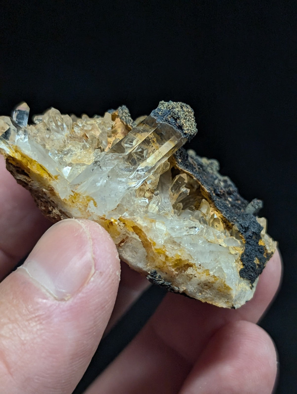 A translucent quartz crystal cluster with golden-yellow veining and dark mineral matrix, held in hand.