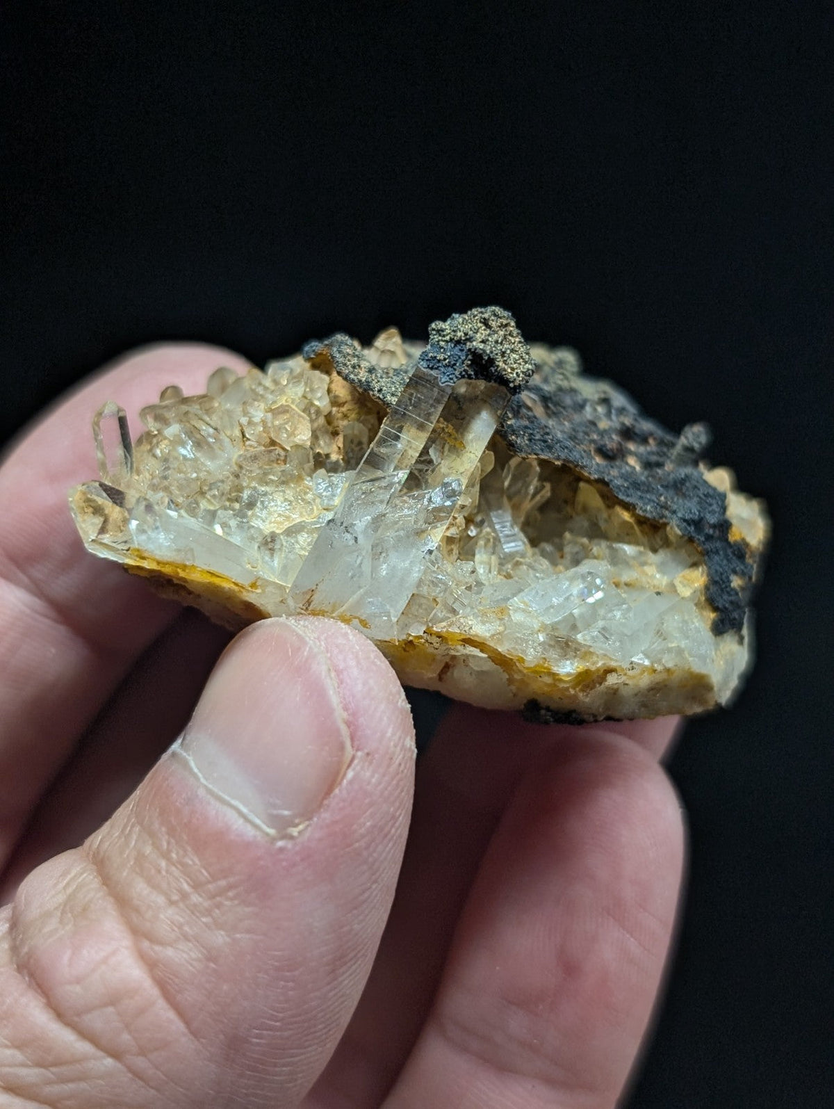 A translucent quartz crystal cluster emerging from a yellowish, earthy matrix with dark mineral patches.