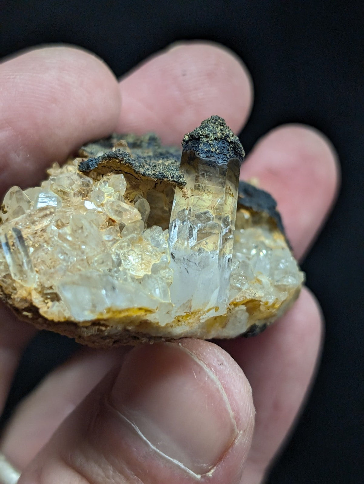 A translucent quartz crystal cluster with a clear, faceted central column and surrounding smaller crystals, set against a dark matrix.
