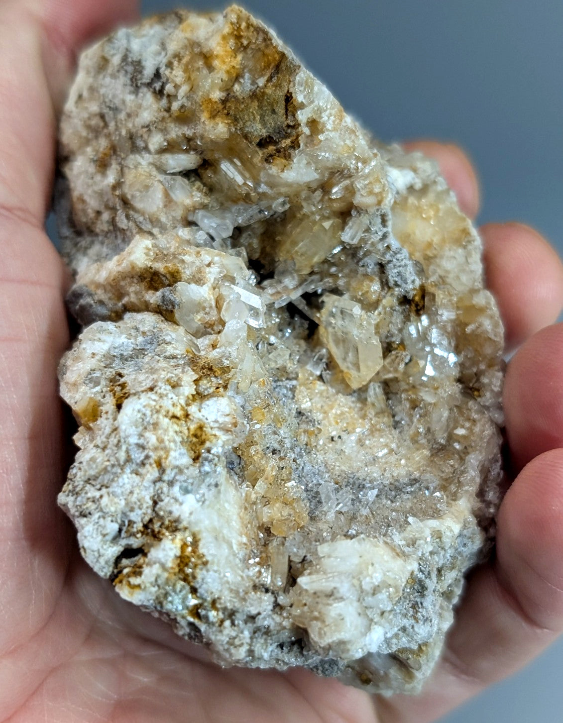 A hand holds a quartz crystal cluster with golden-yellow and grayish solution quartz and cookeite from Arkansas