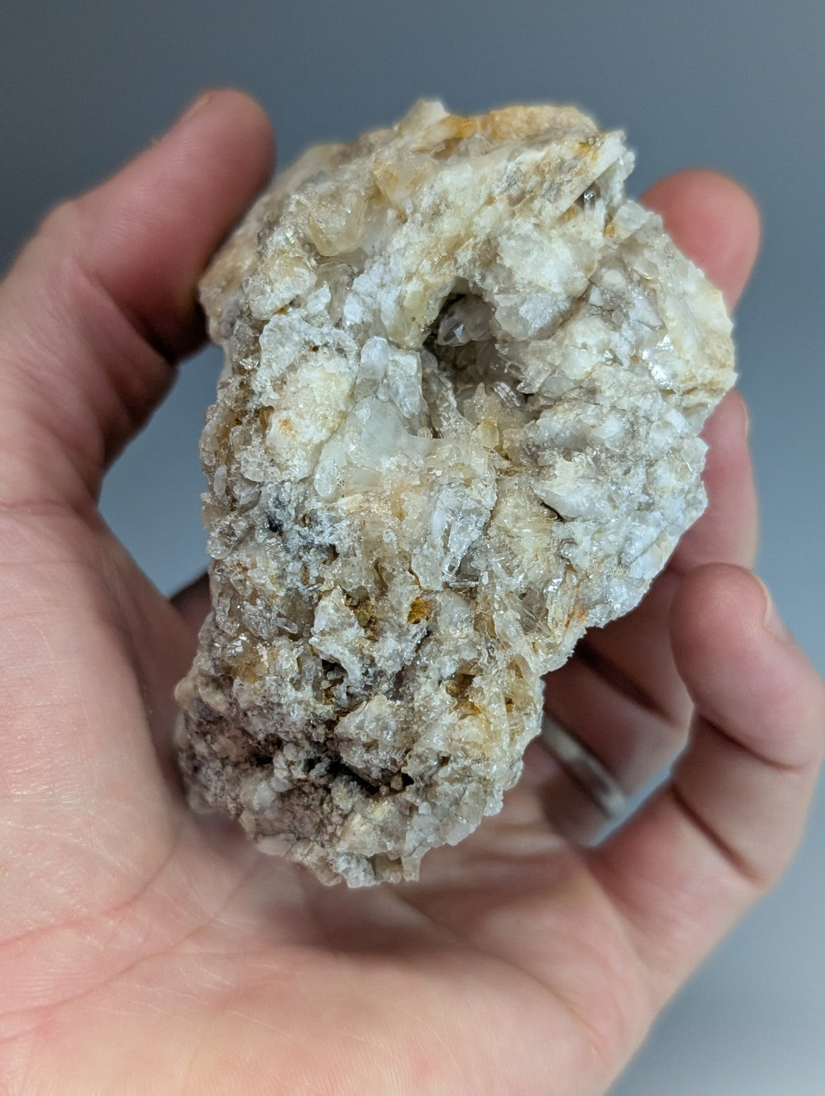 A hand holds a rough quartz crystal cluster with white and pale yellow formations from Saline County Arkansas