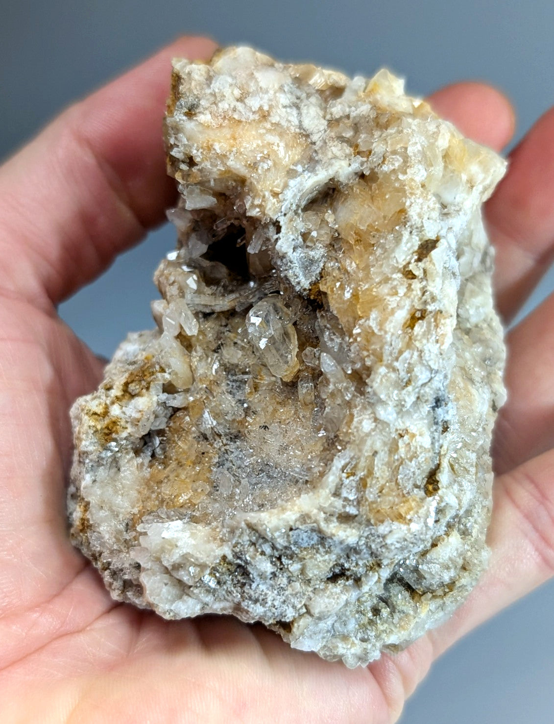 A hand holds a rough quartz crystal cluster with solution quartz and cookeite from Saline County Arkansas