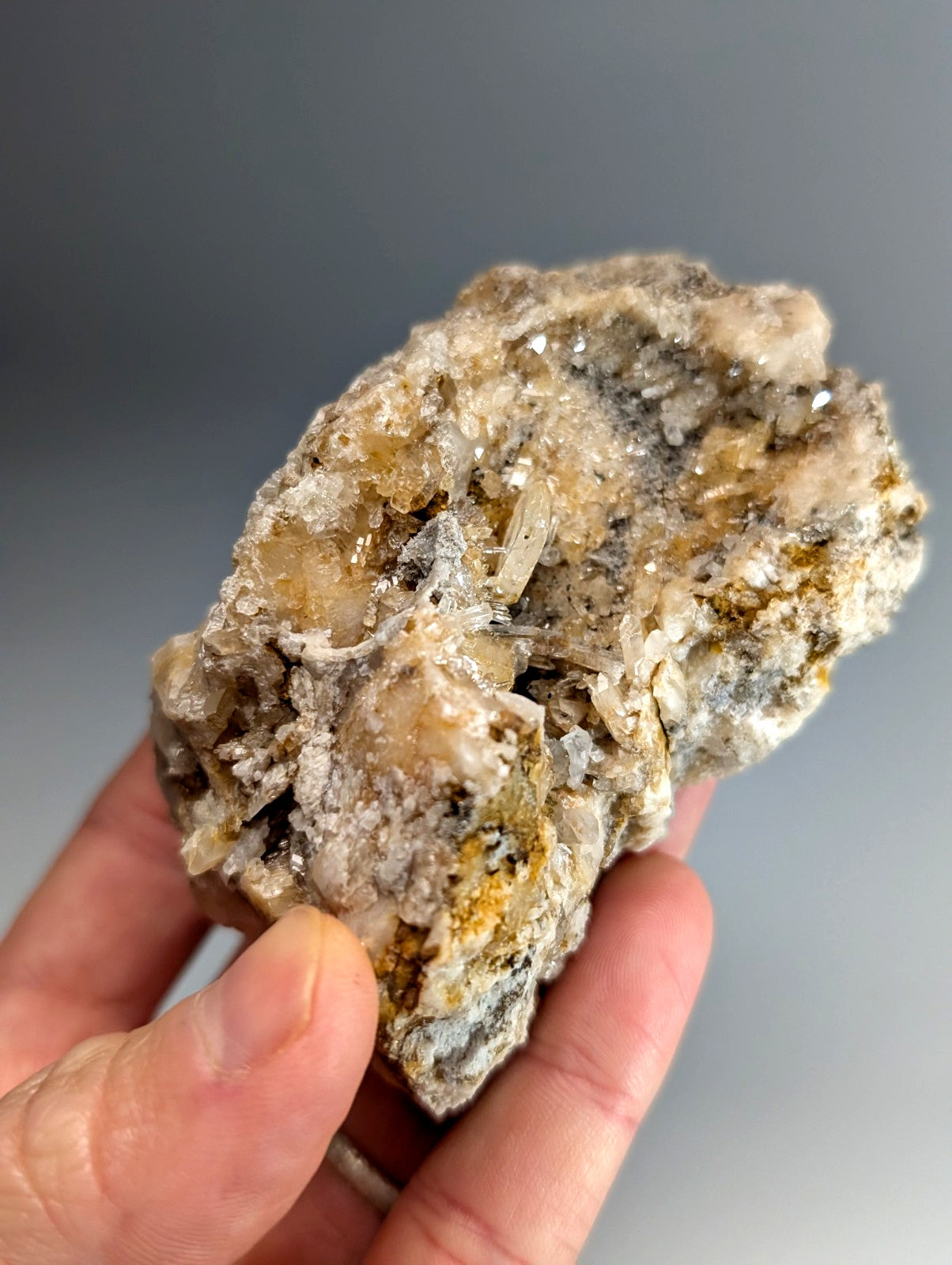 A hand holds a quartz crystal cluster with solution quartz and cookeite in yellow and gray from Saline County Arkansas