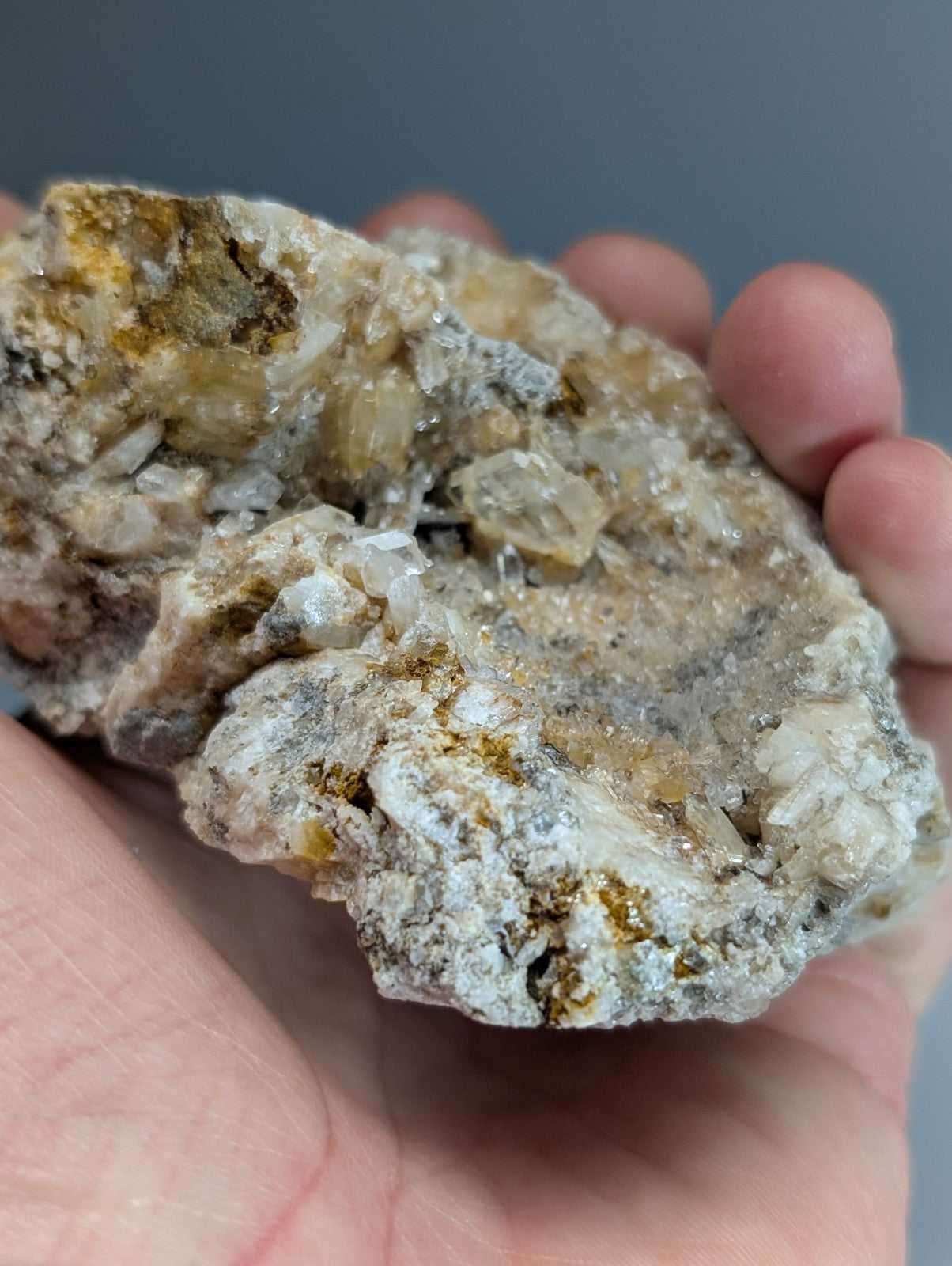 A hand holds a quartz crystal cluster with translucent solution quartz and cookeite in gray and yellowish matrix from Arkansas