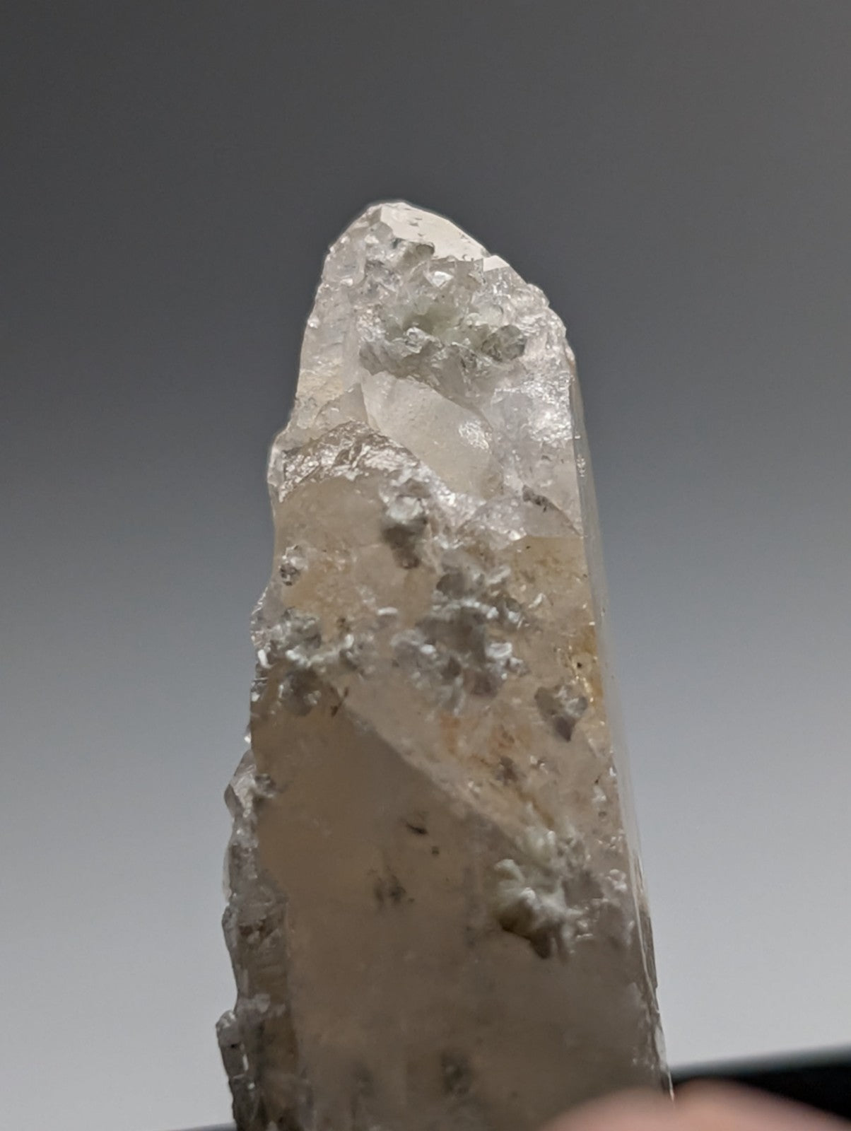 A translucent pale quartz crystal point with rough jagged surface and uv reactive cookeite from saline county arkansas usa