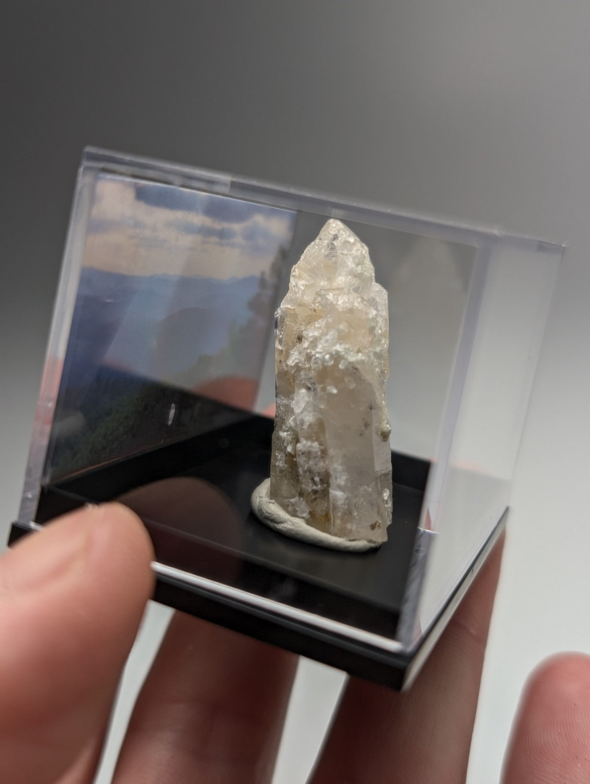 A translucent faceted quartz crystal point with uv reactive cookeite and natural inclusions in a clear acrylic case