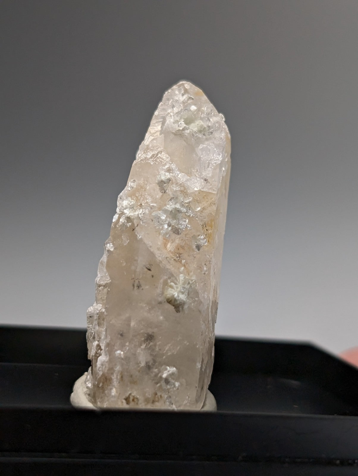 A translucent pale quartz crystal point with uv reactive cookeite and a rough faceted surface from arkansas usa