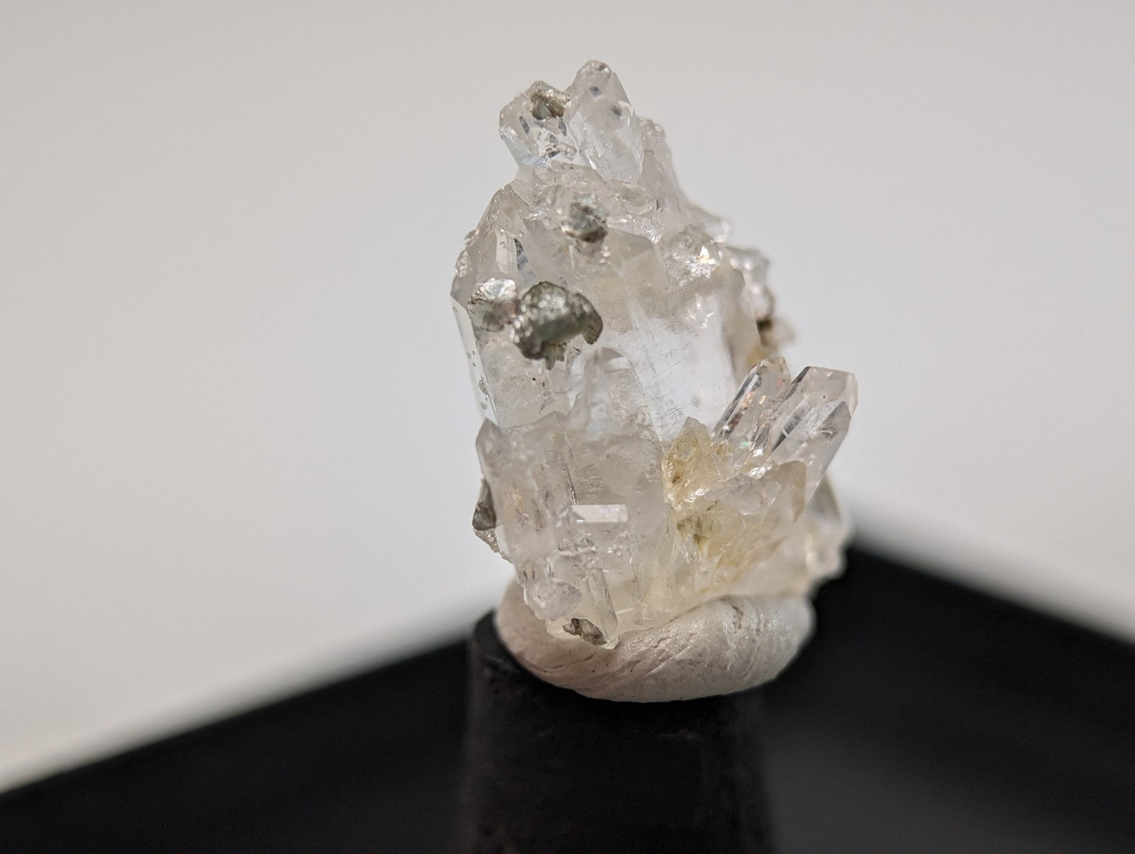 Clear quartz crystal cluster with metallic inclusions, mounted on a black display stand.