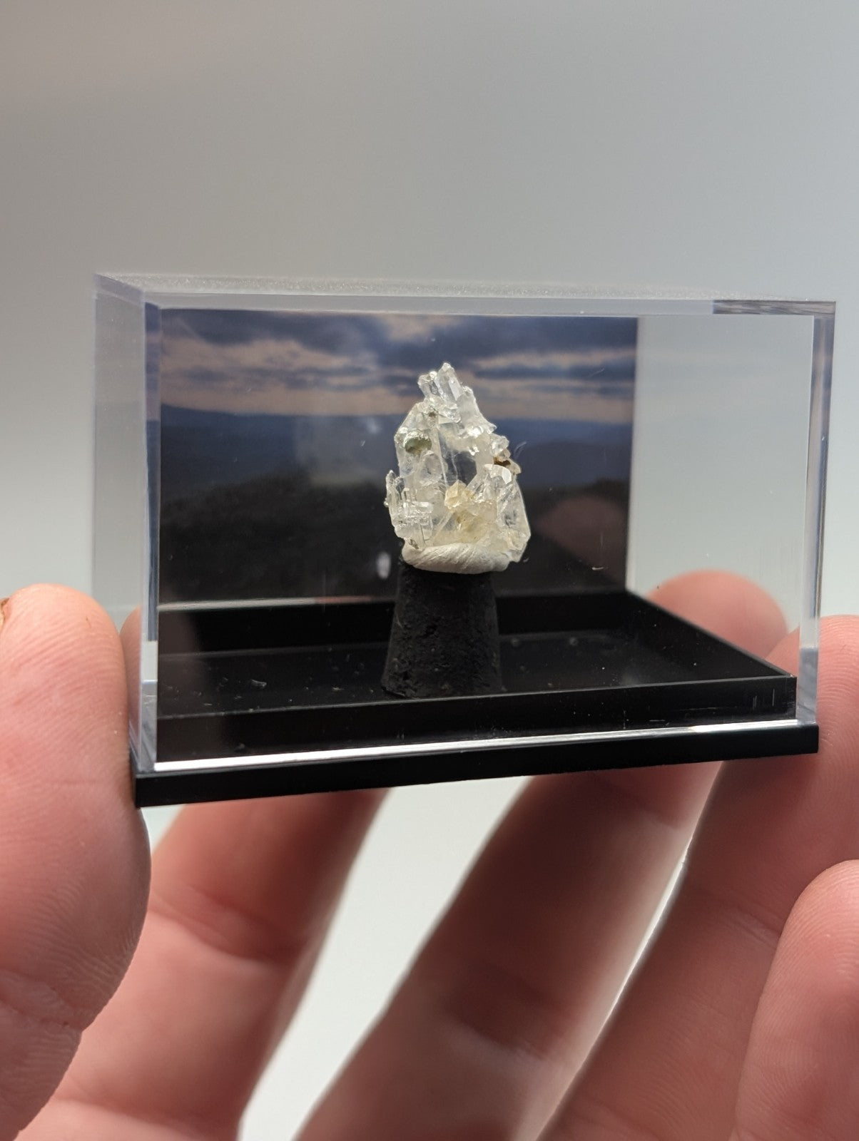 A translucent, crystalline mineral specimen with a rough, jagged surface and subtle internal inclusions is displayed within a clear acrylic display case.