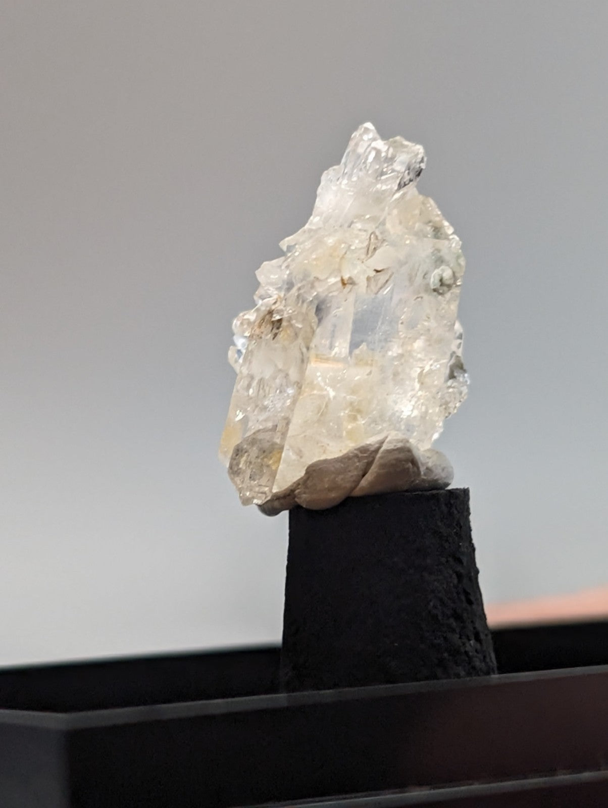 A translucent, faceted crystal cluster with a clear and milky white appearance rests on a black pedestal.