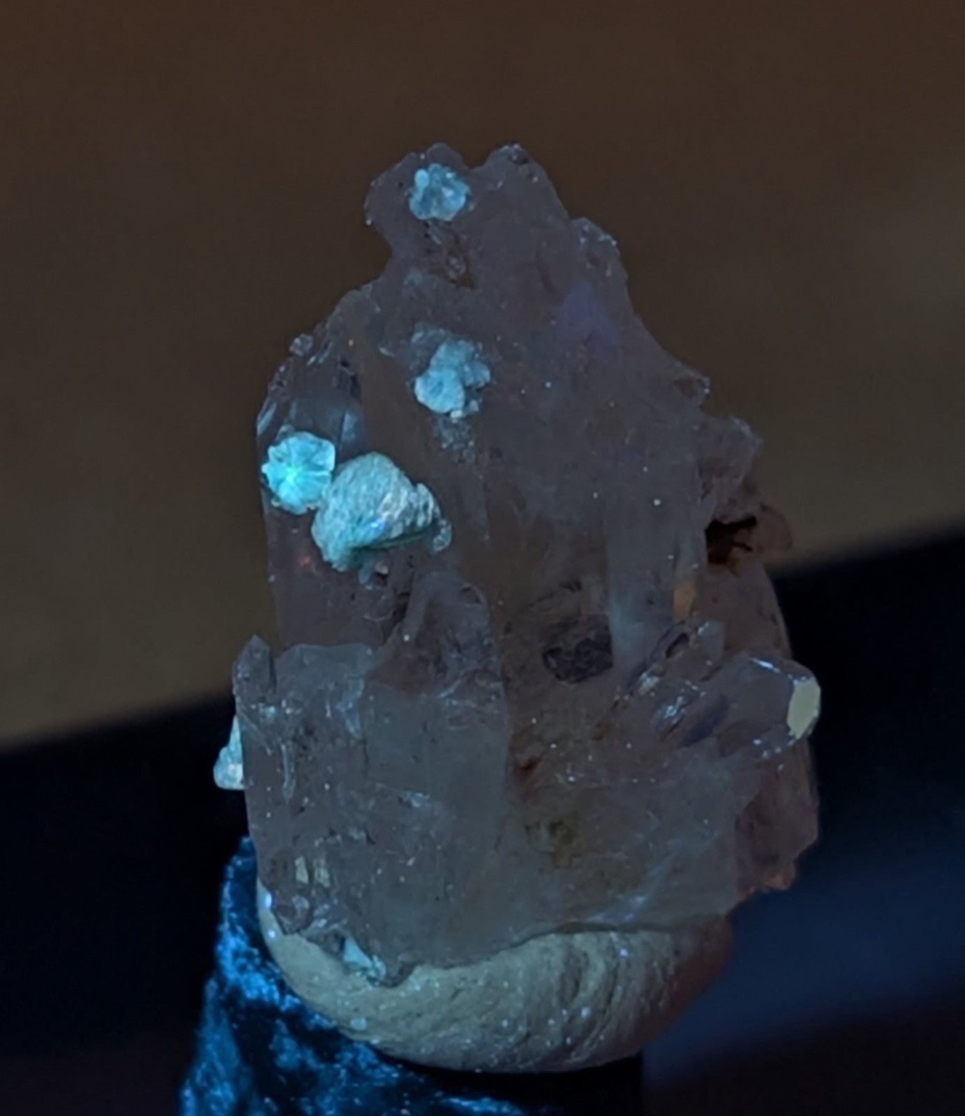 A translucent quartz crystal cluster with embedded turquoise-colored mineral formations, mounted on a textured base.