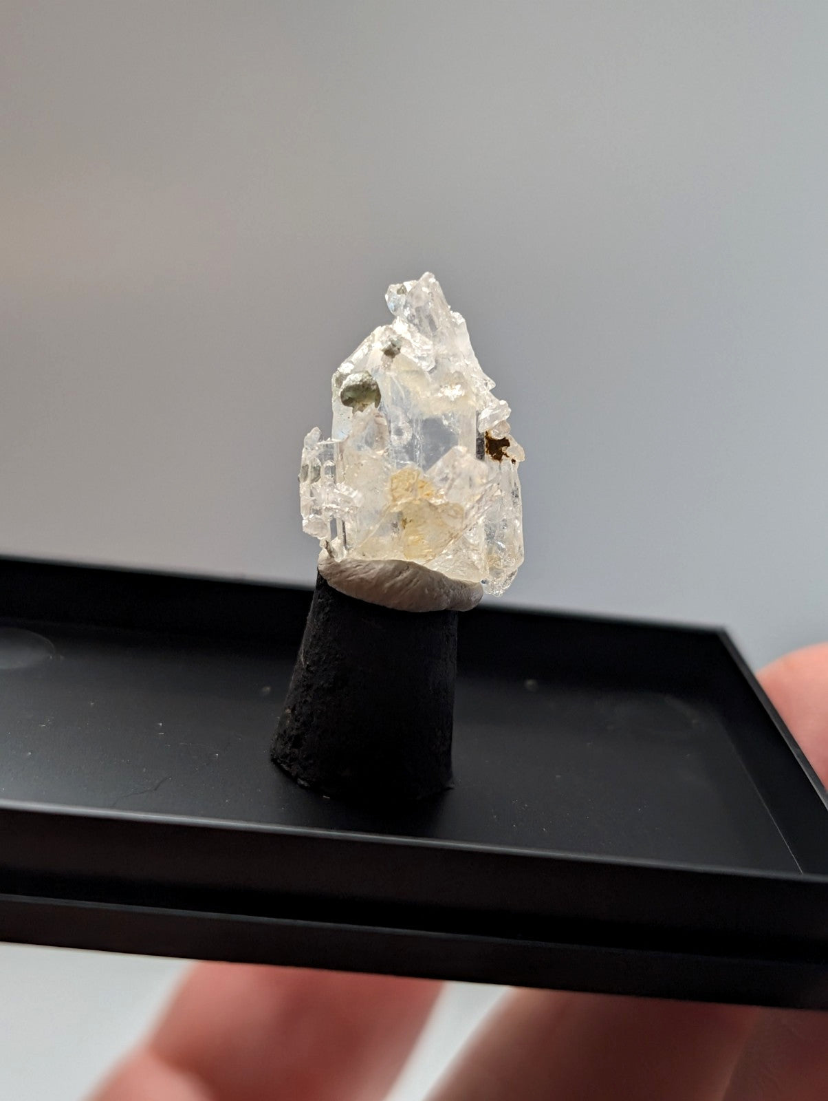 A clear, faceted crystal mineral specimen with embedded green and yellow inclusions.