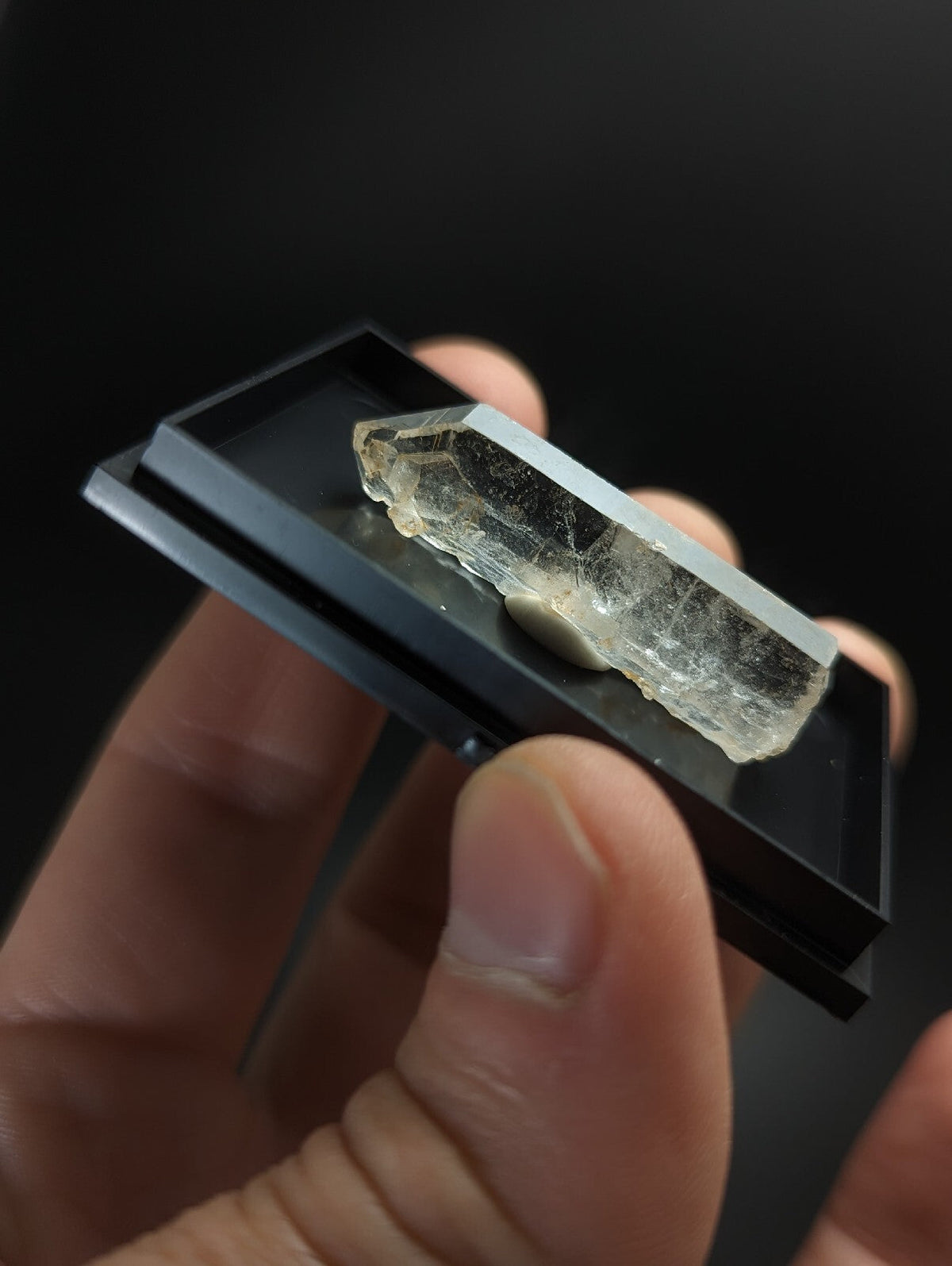 A translucent, pale yellowish crystal with a rough, faceted surface and visible internal inclusions rests on a sleek black display tray.