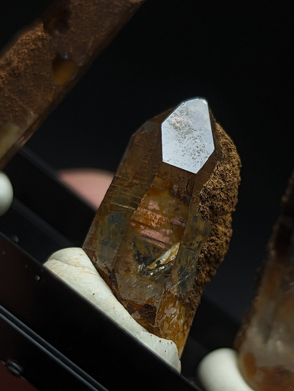 A translucent amber-colored crystal with a pointed, faceted top and rough brown matrix base.