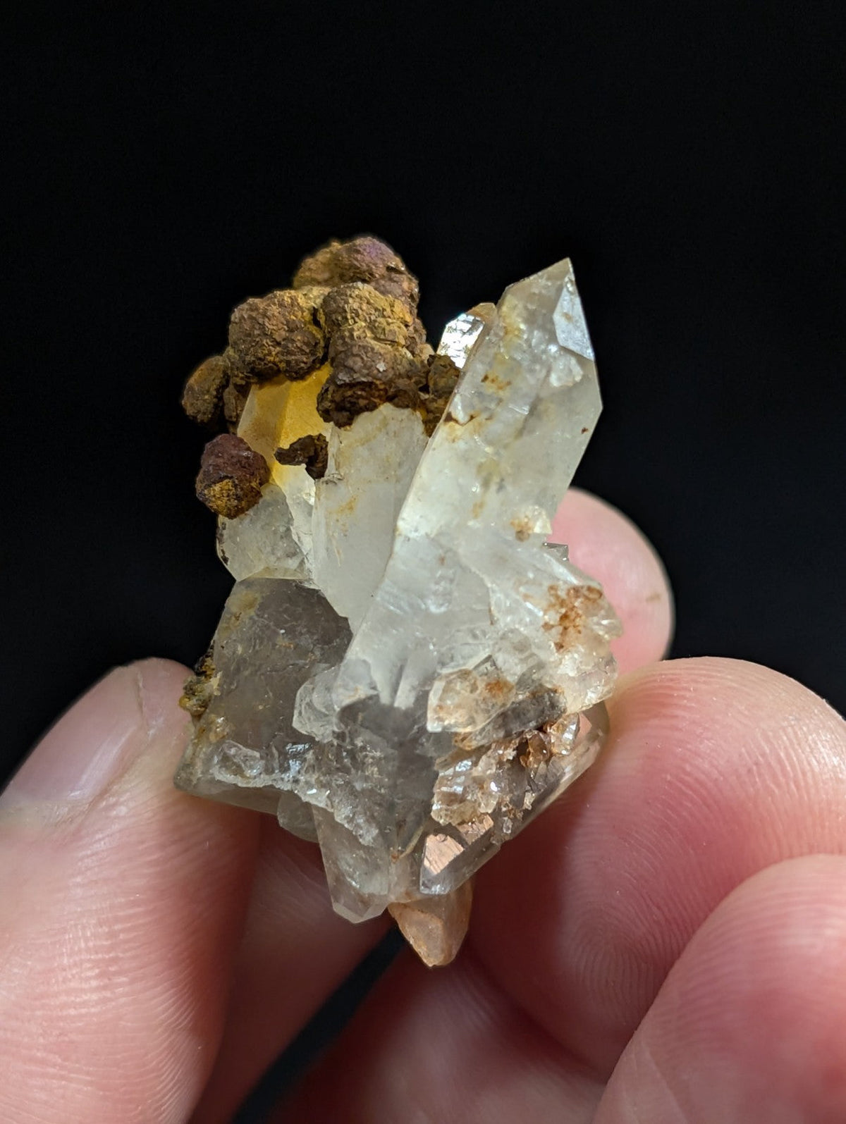 A translucent quartz crystal cluster with brownish mineral inclusions, held gently between fingers.