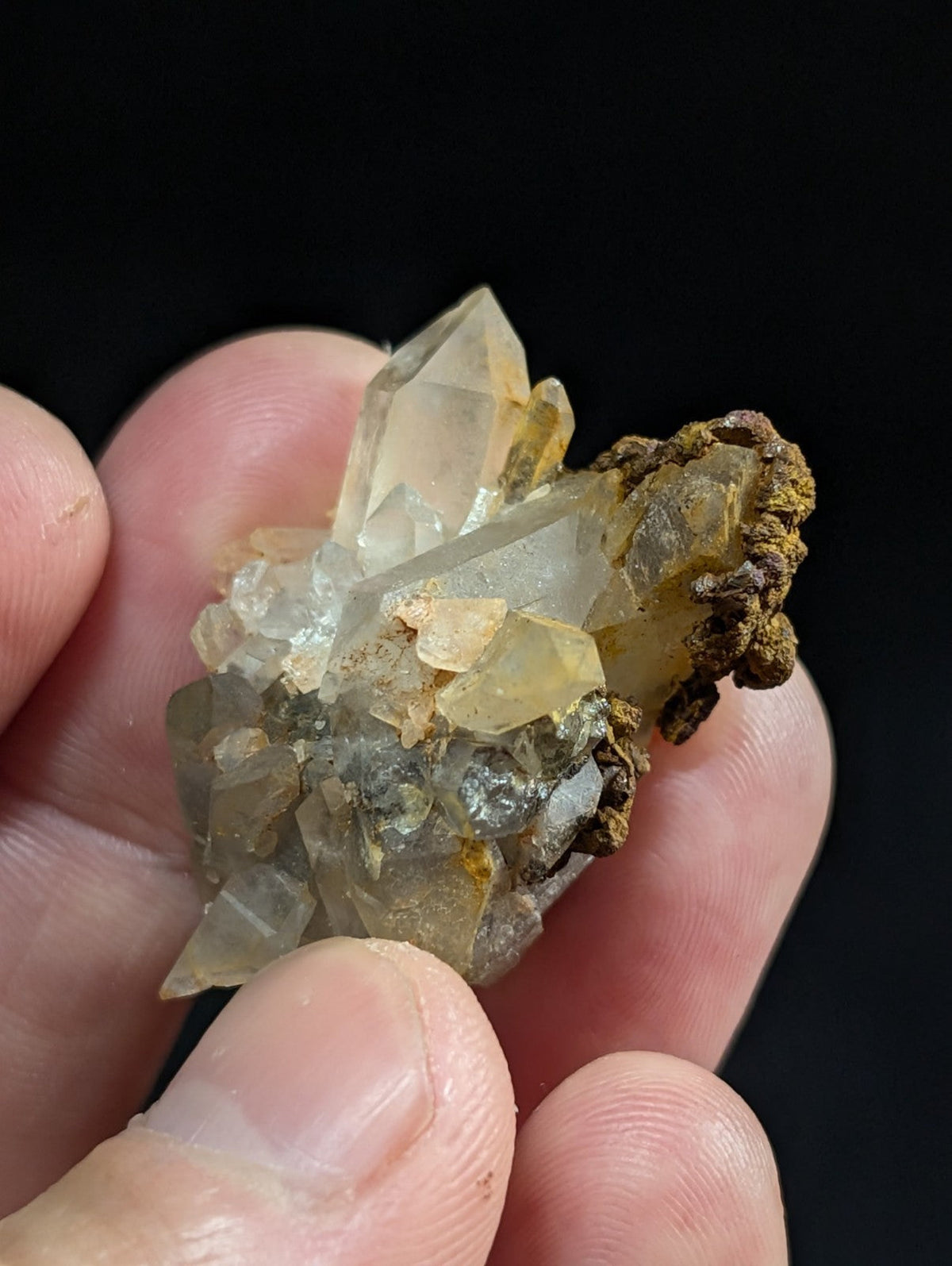 A cluster of translucent, pale yellow and clear quartz crystals with a rough, earthy brown matrix.