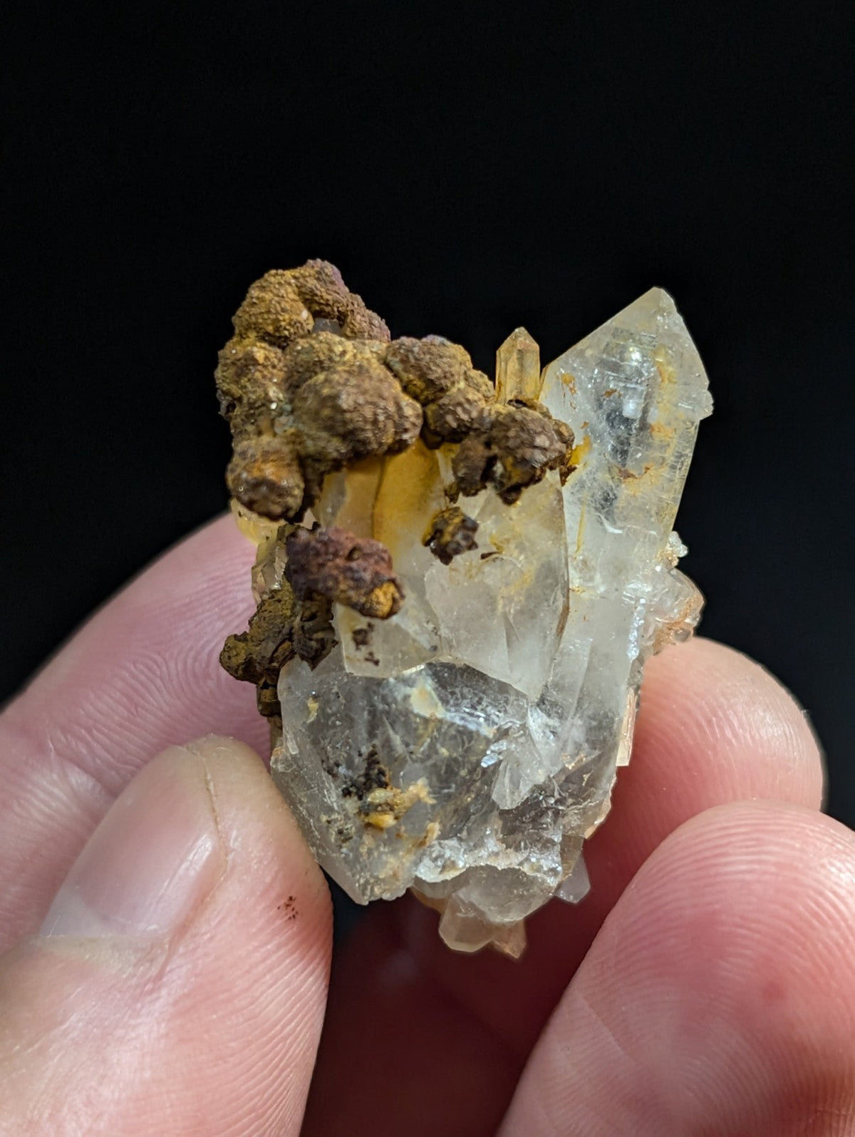 A translucent, crystalline mineral specimen with clear facets and brownish-yellow earthy matrix.