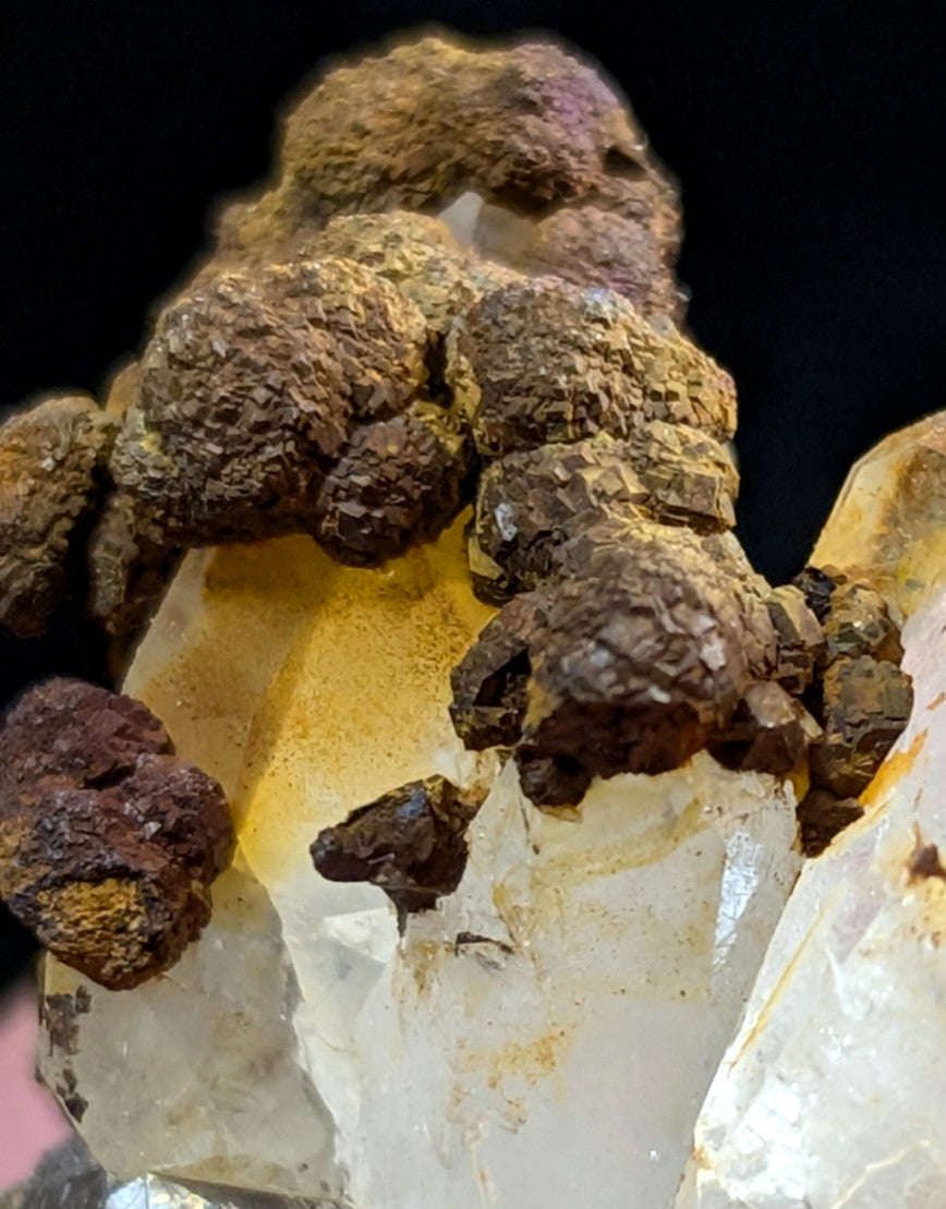A translucent quartz crystal formation with earthy brown and yellow mineral deposits clinging to its surface.