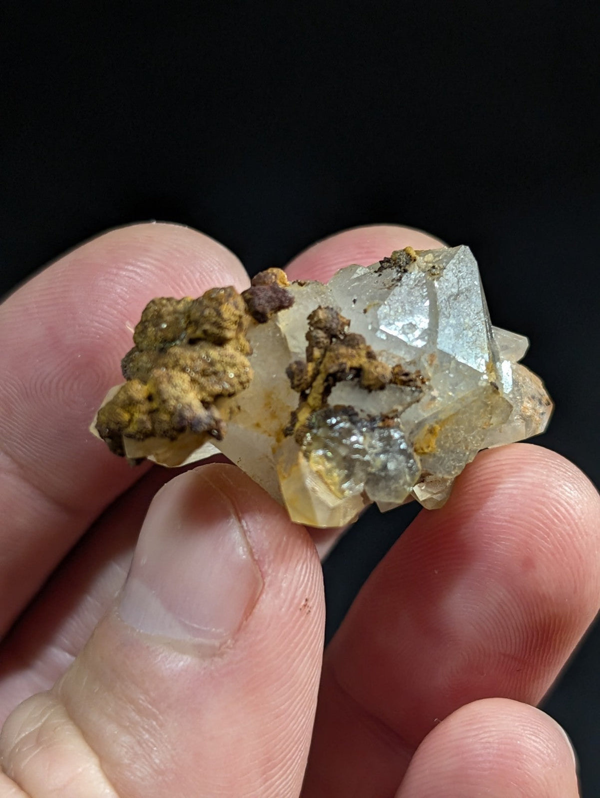 A translucent, crystalline mineral specimen with a pale yellowish hue and sharp geometric facets, partially encrusted with earthy brown and gray material.