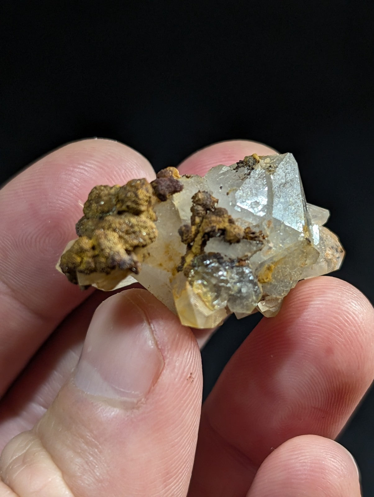 A translucent, crystalline mineral specimen with a pale yellowish hue and sharp geometric facets, partially encrusted with earthy brown and gray material.