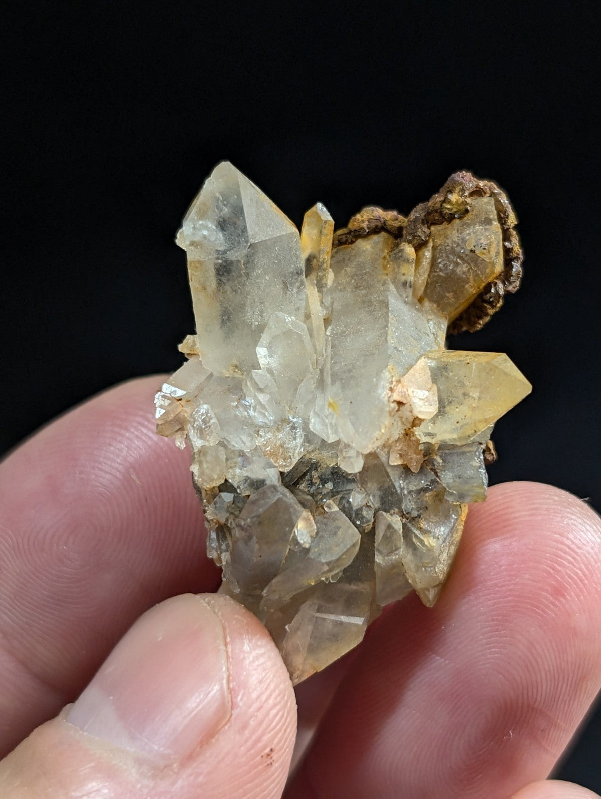 A cluster of translucent, pale yellow quartz crystals with sharp facets and a rough, earthy matrix.