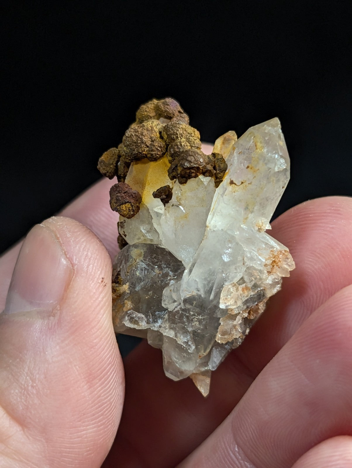 A translucent quartz crystal cluster with brownish-yellow mineral inclusions, held gently between fingers.