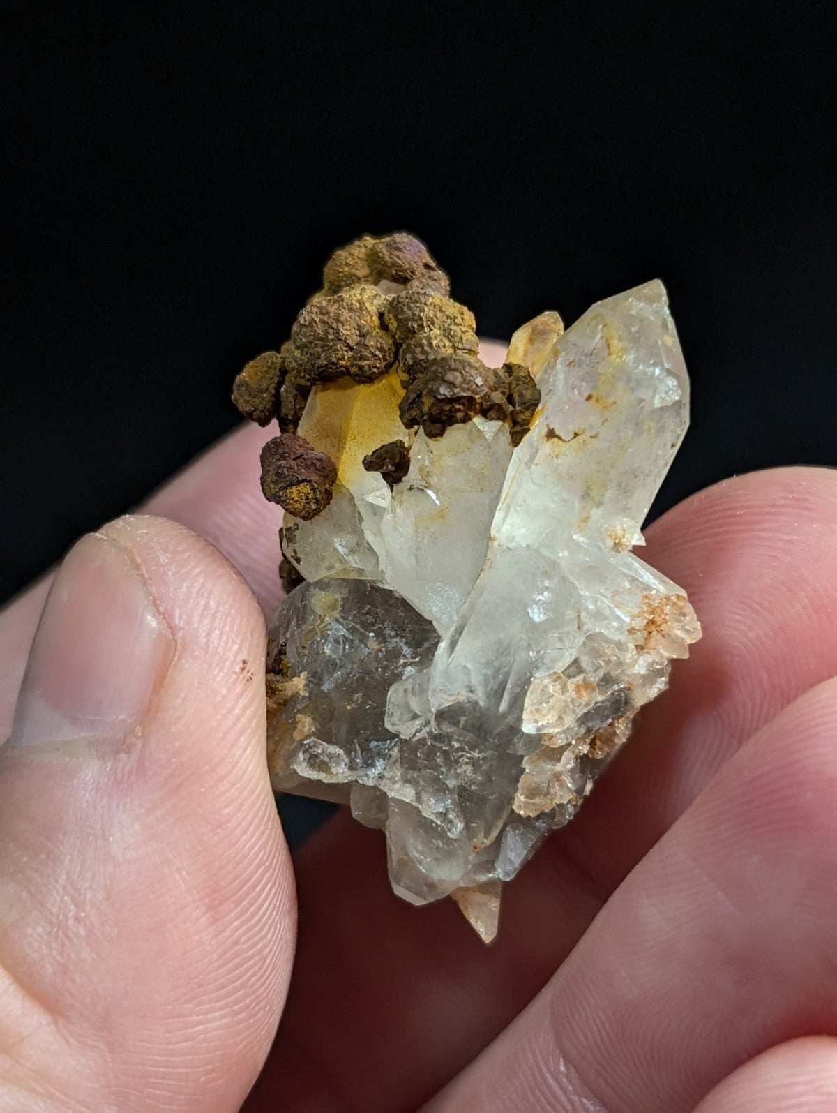 A translucent quartz crystal cluster with brownish-yellow mineral inclusions, held gently between fingers.