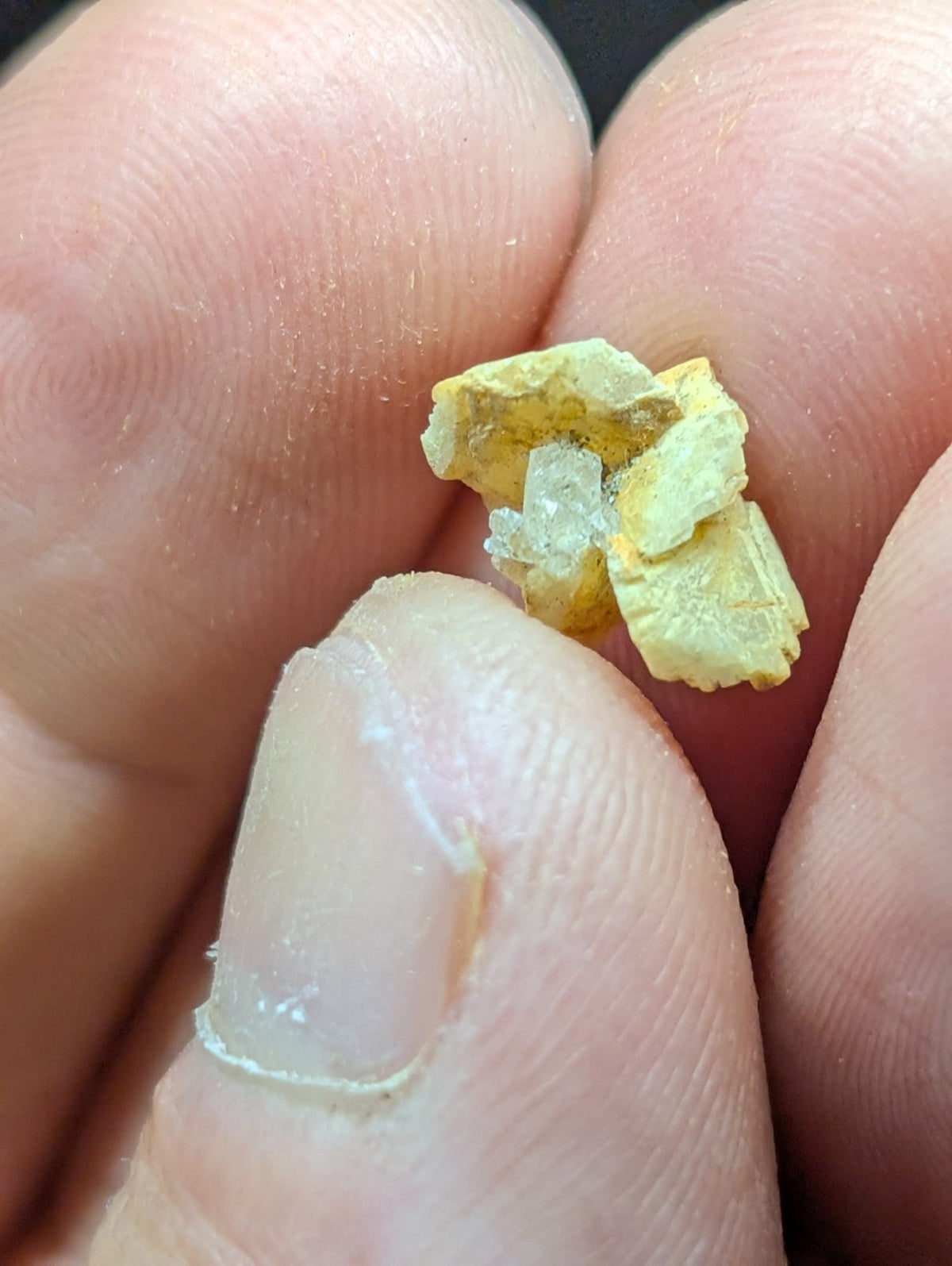 A small, irregularly shaped piece of yellowish mineral with translucent crystalline inclusions nestled between fingers.