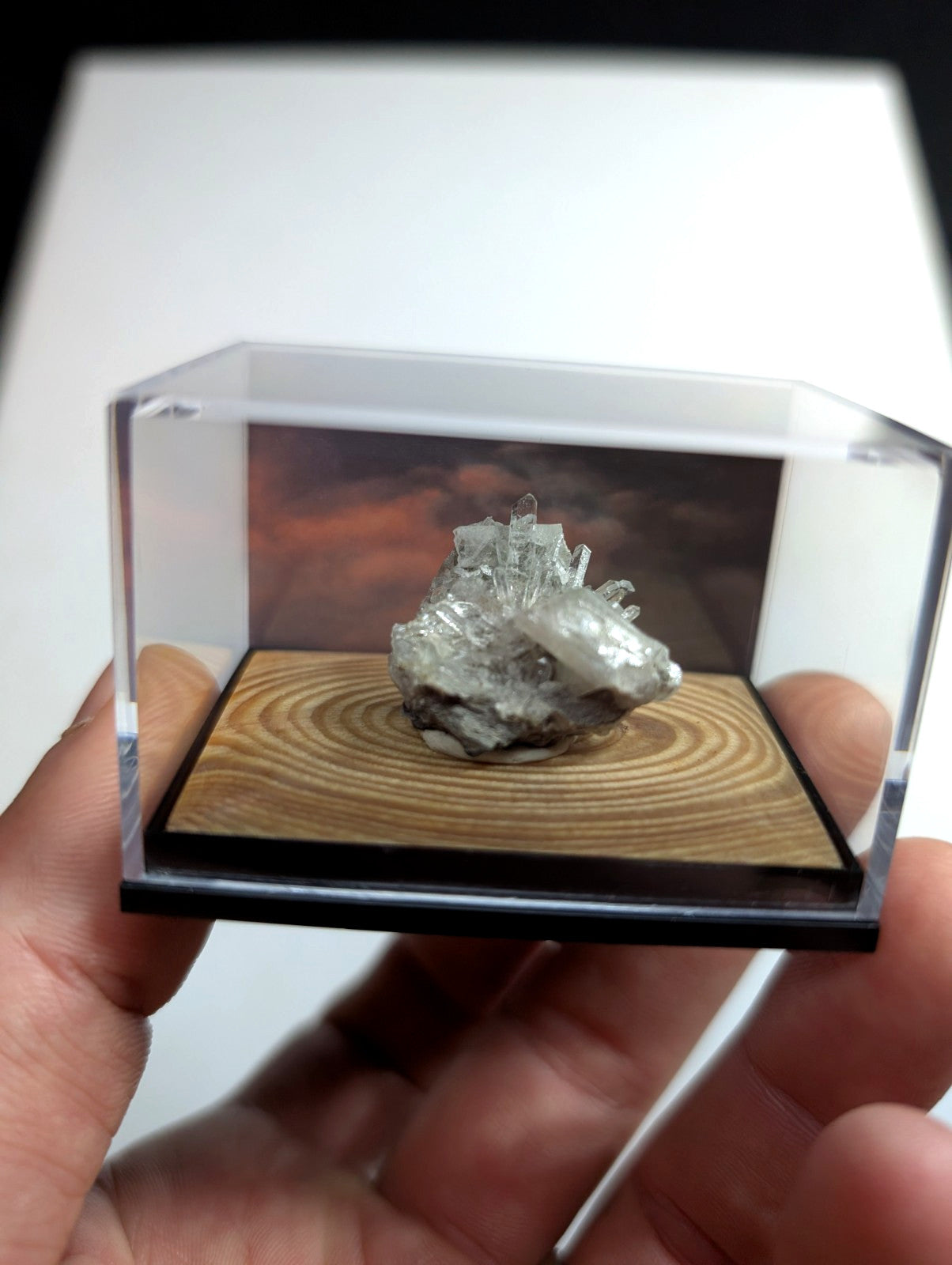A translucent, crystalline mineral specimen with sharp facets and a pale grayish hue is displayed inside a clear acrylic display case.