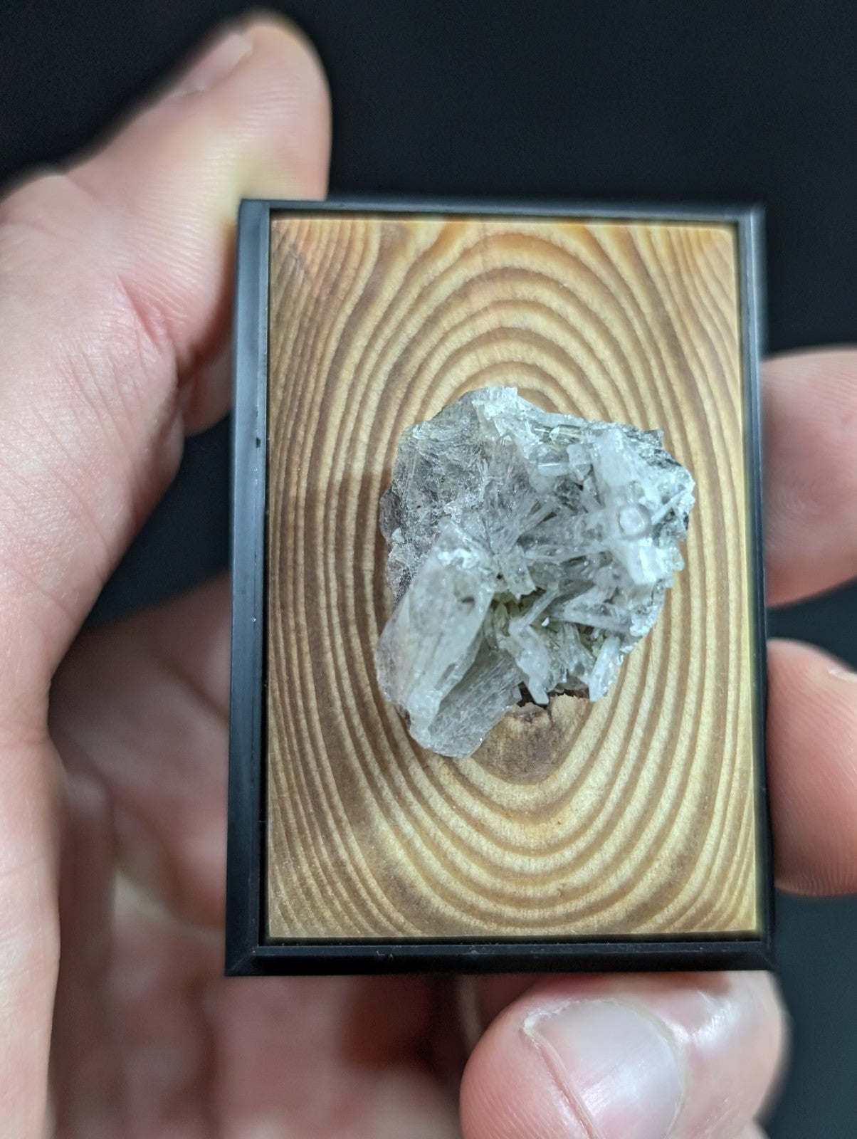 A clear, faceted quartz crystal cluster mounted in a black-framed wooden display.