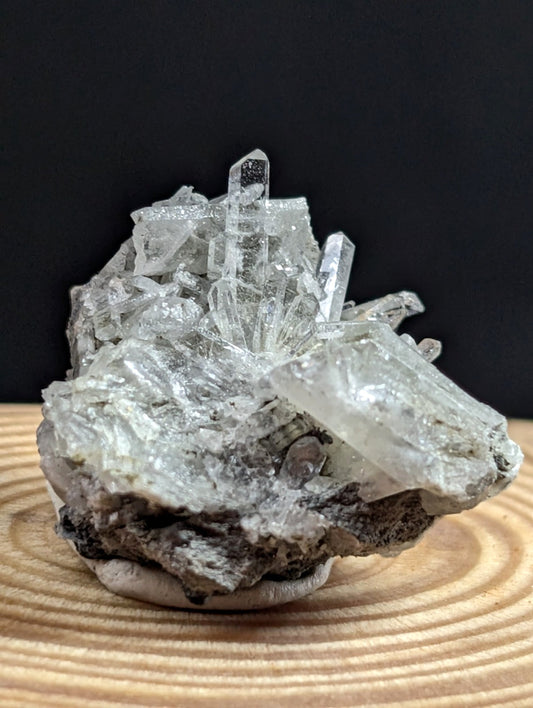 A clear quartz crystal cluster with sharp, translucent points emerging from a dark gray rock base.