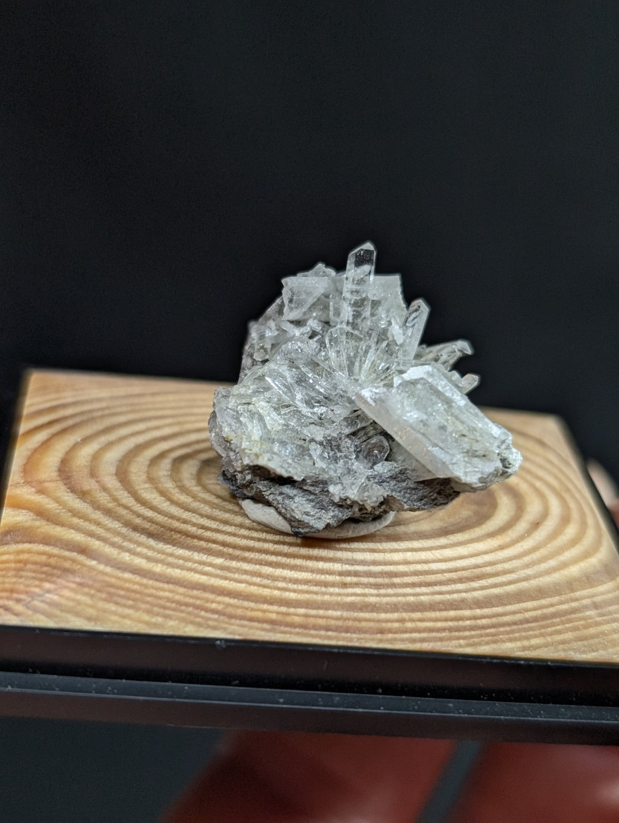 A translucent quartz crystal cluster with sharp, faceted points emerging from a rough, grayish rock base.