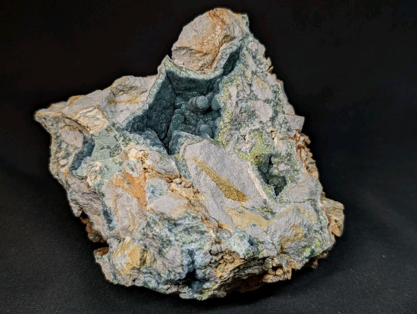 A rugged, irregularly shaped mineral specimen featuring a striking blue-green crystalline interior contrasted against its weathered gray and tan exterior.
