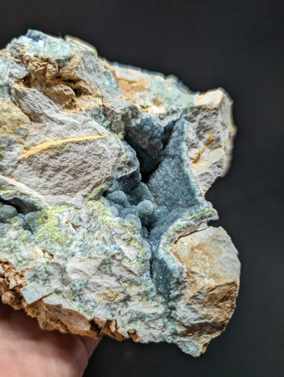 A rugged, irregularly shaped mineral specimen featuring a striking contrast between its rough, earthy-toned matrix and the vibrant blue-green crystalline formations that cluster together in a dense, textured pattern.