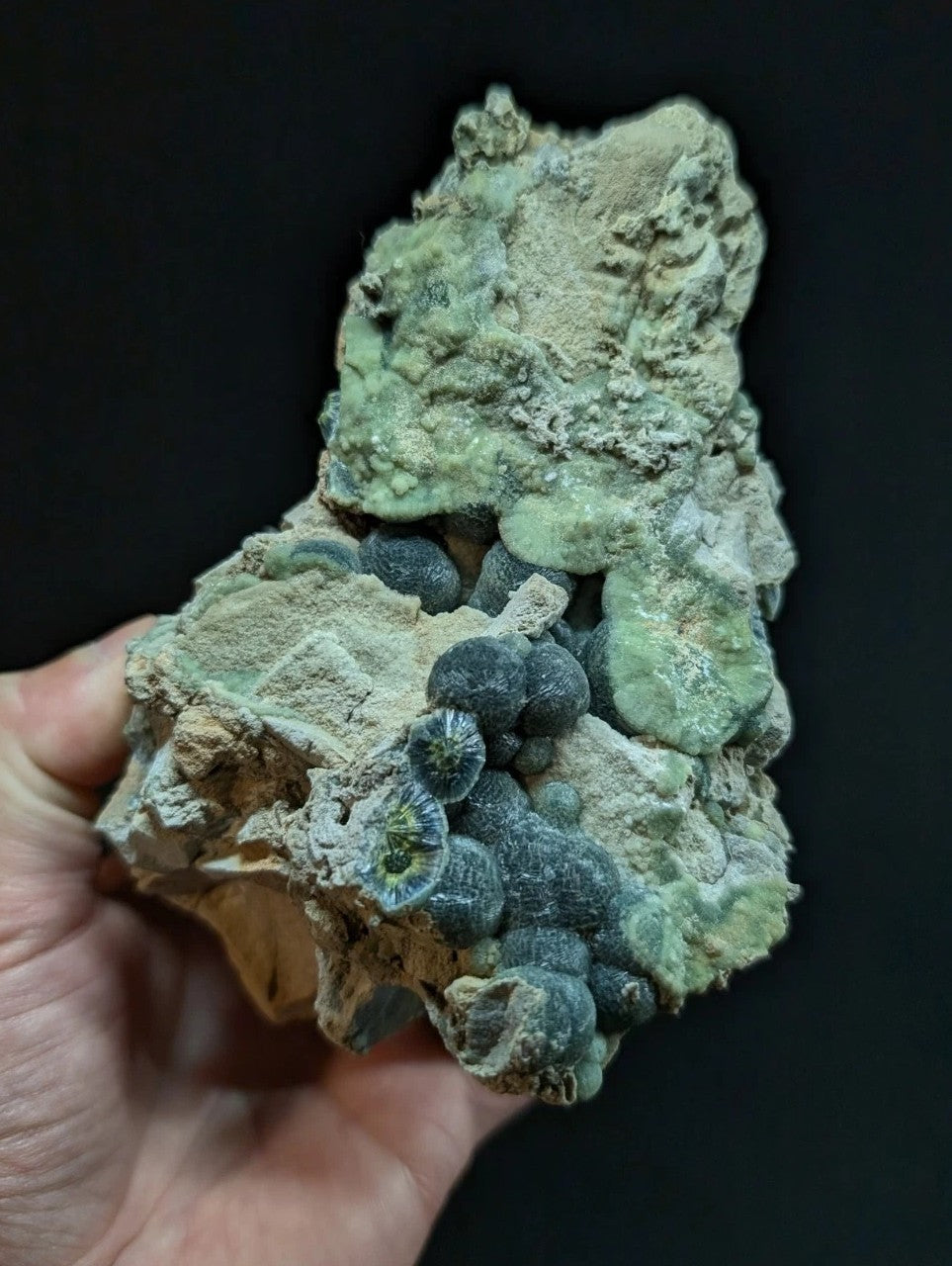 A textured mineral specimen featuring a cluster of dark blue, rounded formations nestled within lighter green and beige crystalline matrix.