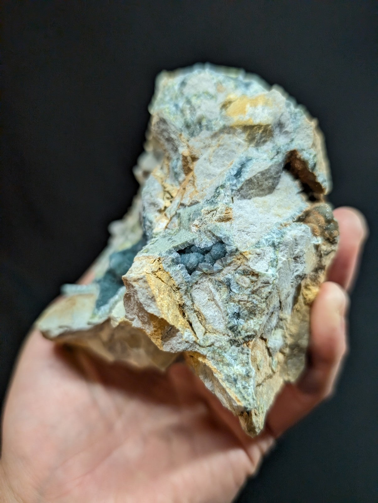 A rugged, irregularly shaped mineral specimen with a mottled surface of grayish-white and patches of blue-green, accented by streaks of yellow.