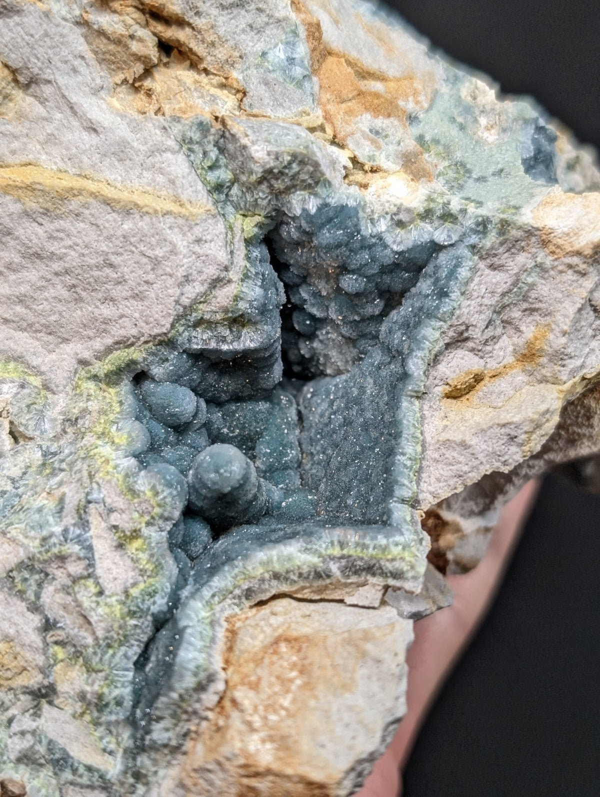 A striking blue-green mineral specimen with a crystalline, bubbly texture nestled within a rugged, multi-toned rock matrix.