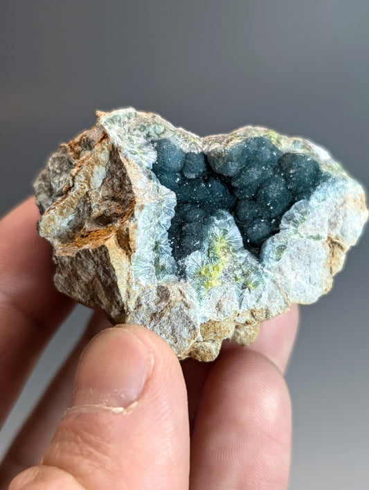 A hand holds a rare blue and green wavellite geode with dark blue druzy crystals from Garland County Arkansas