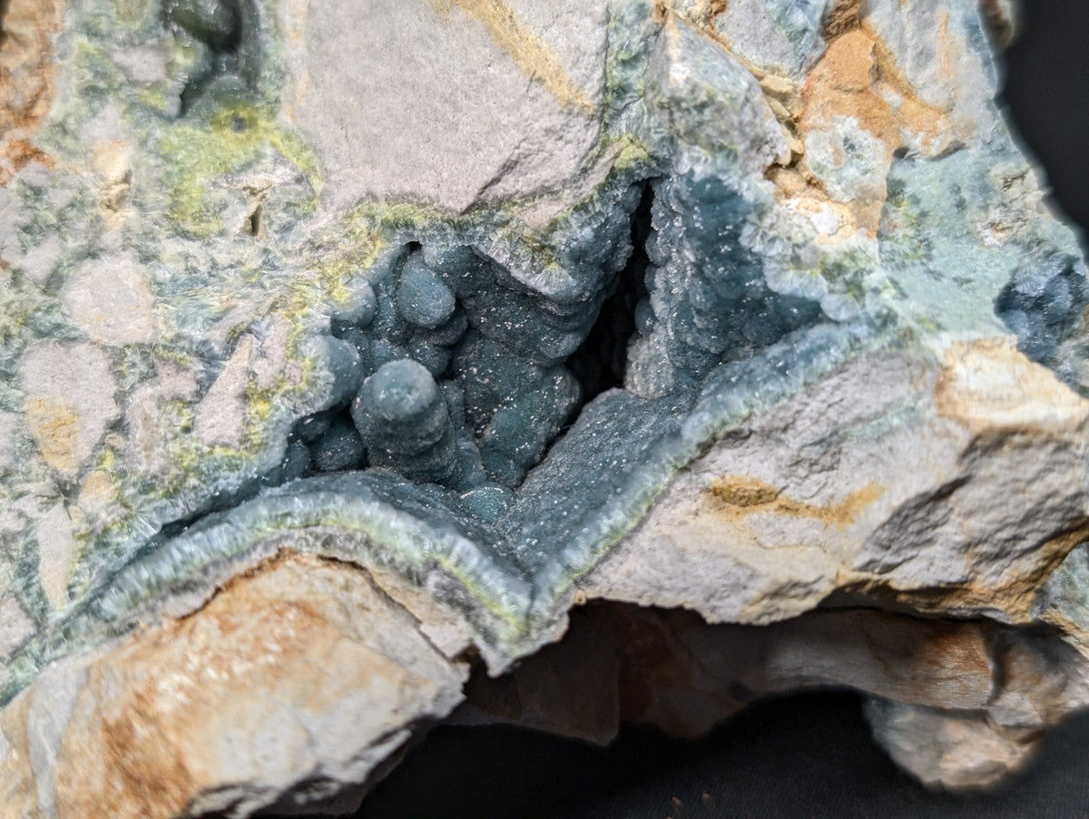 A striking blue-green mineral specimen featuring clustered, rounded crystals nestled within a rugged matrix of gray and tan rock.