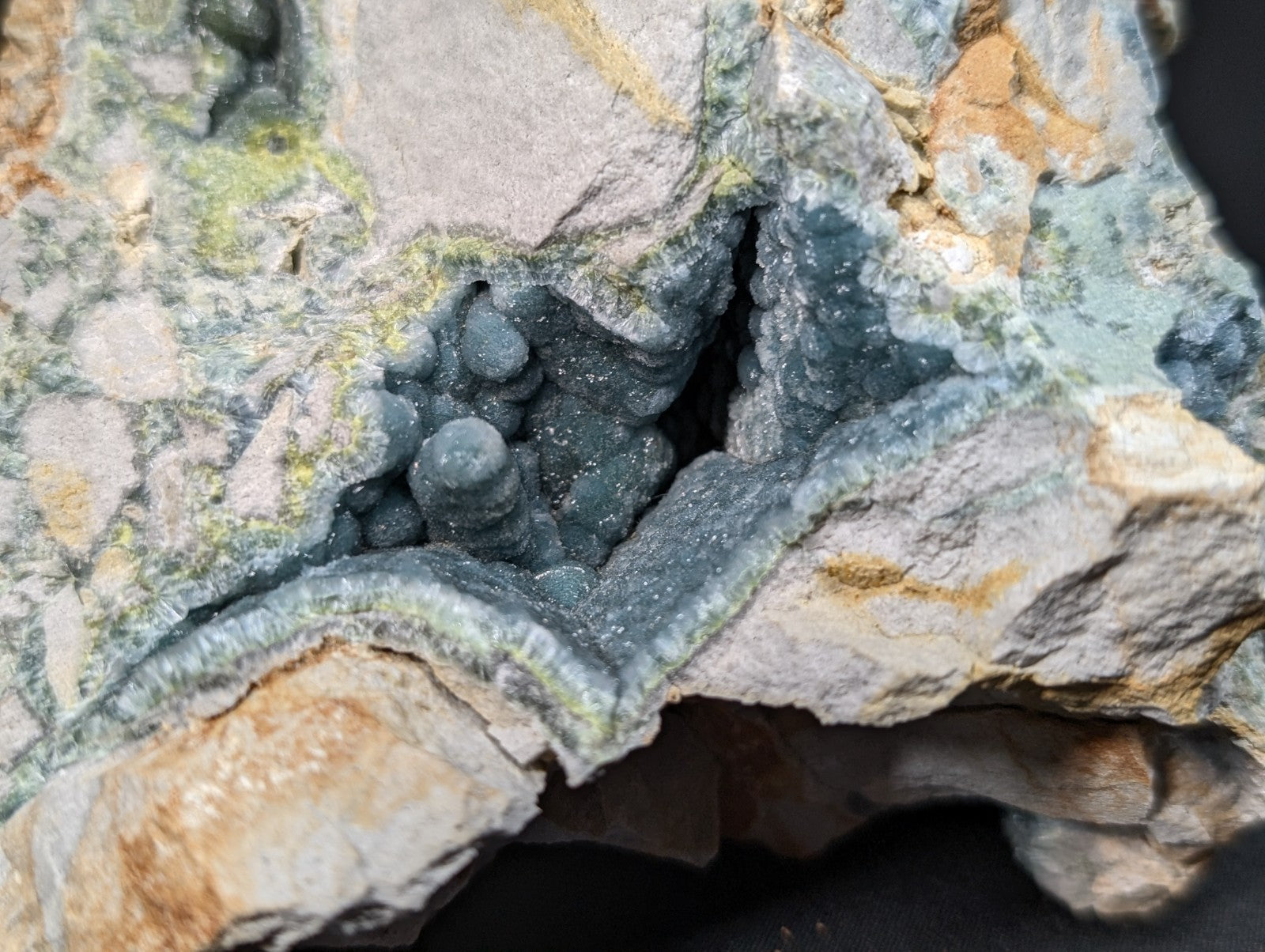A striking blue-green mineral specimen featuring clustered, rounded crystals nestled within a rugged matrix of gray and tan rock.