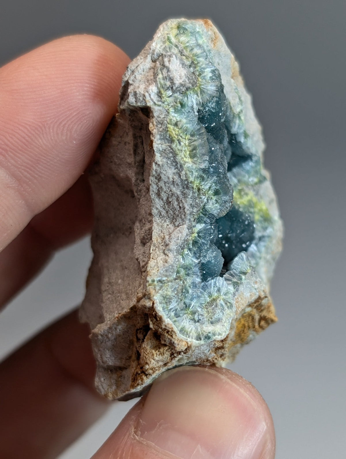 A hand holds a rare blue and green wavellite geode with translucent crystals in a rough brown rock matrix from Garland County Arkansas