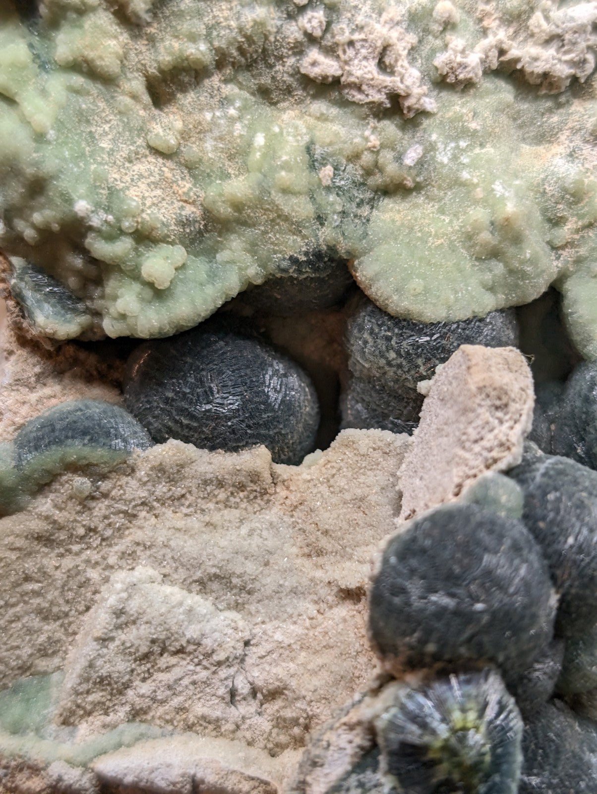 Dark, spherical stone formations nestled among light green and beige mineral deposits.