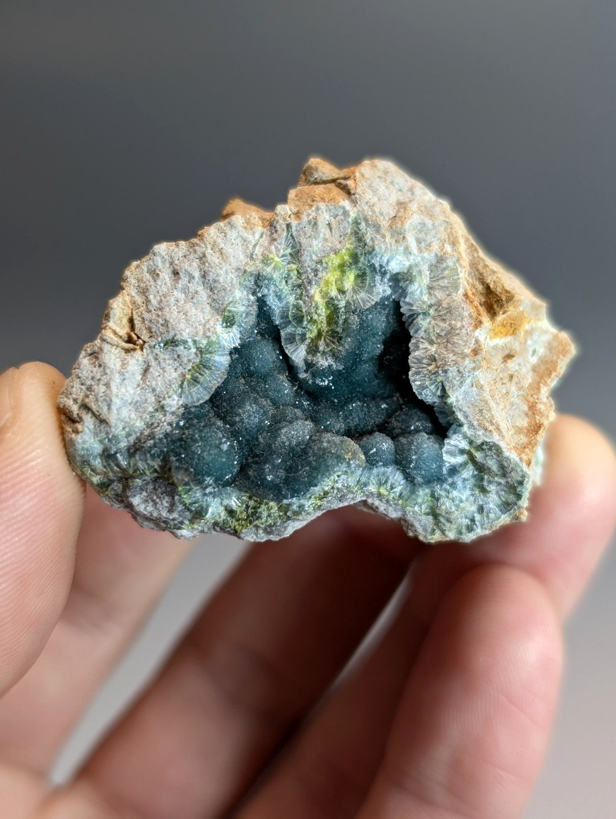 A hand holds a rare blue and green wavellite geode with deep crystalline formations from Garland County Arkansas