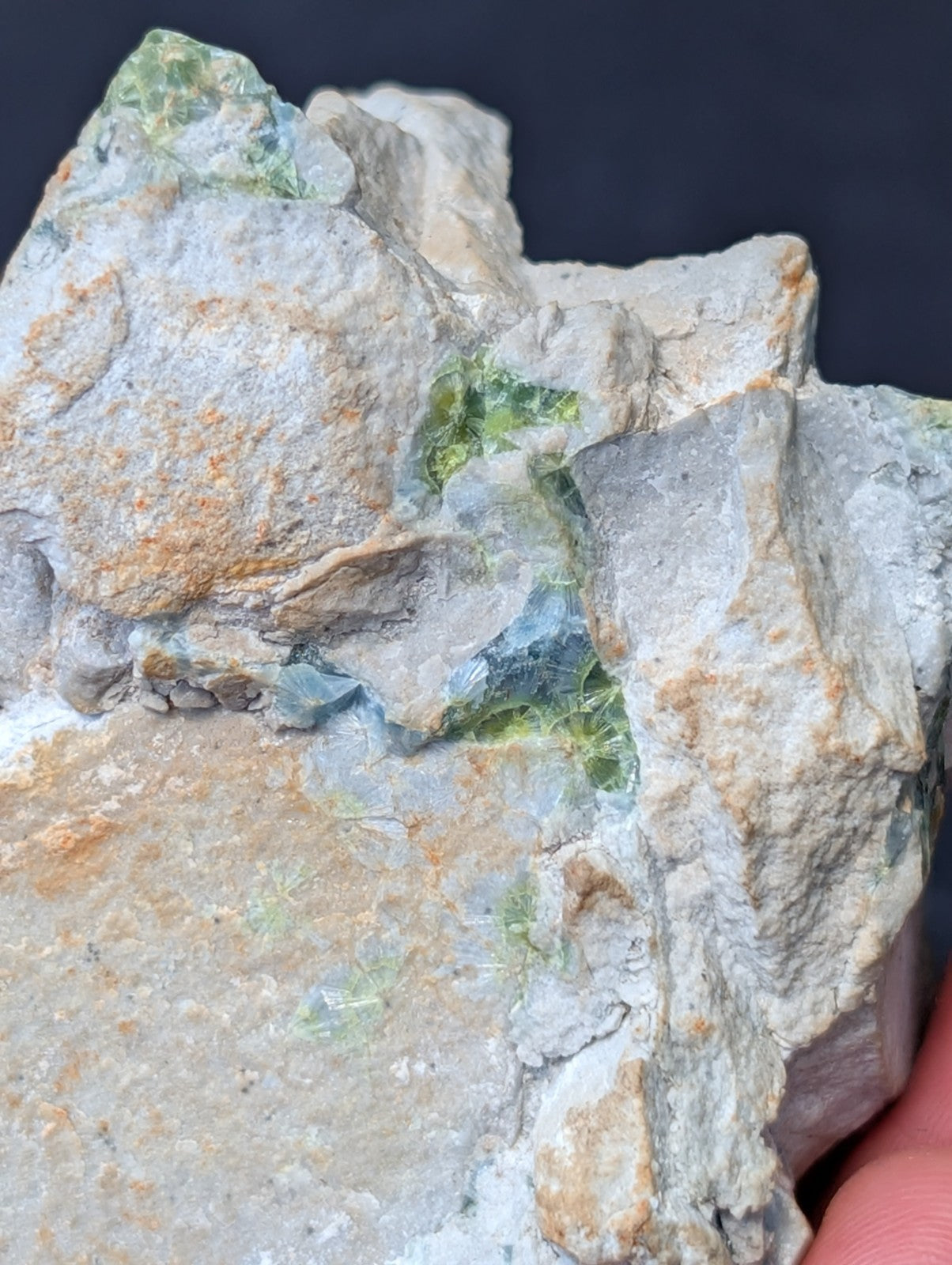 A rough, irregularly shaped rock specimen featuring patches of translucent green mineral inclusions set against a grayish matrix with subtle orange and blue veining.
