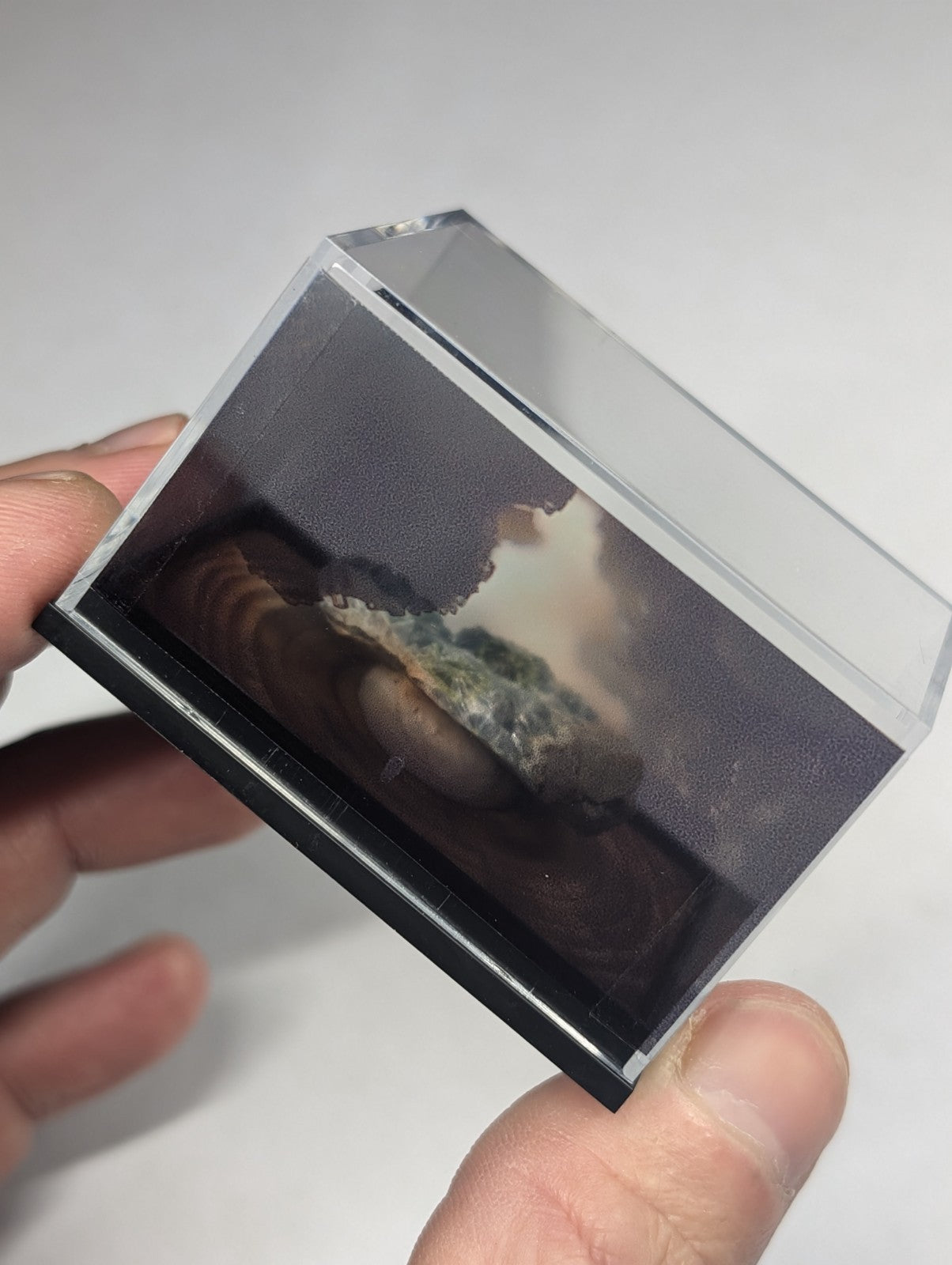 Clear acrylic display case with black base holding a miniature diorama of a rocky, misty landscape.